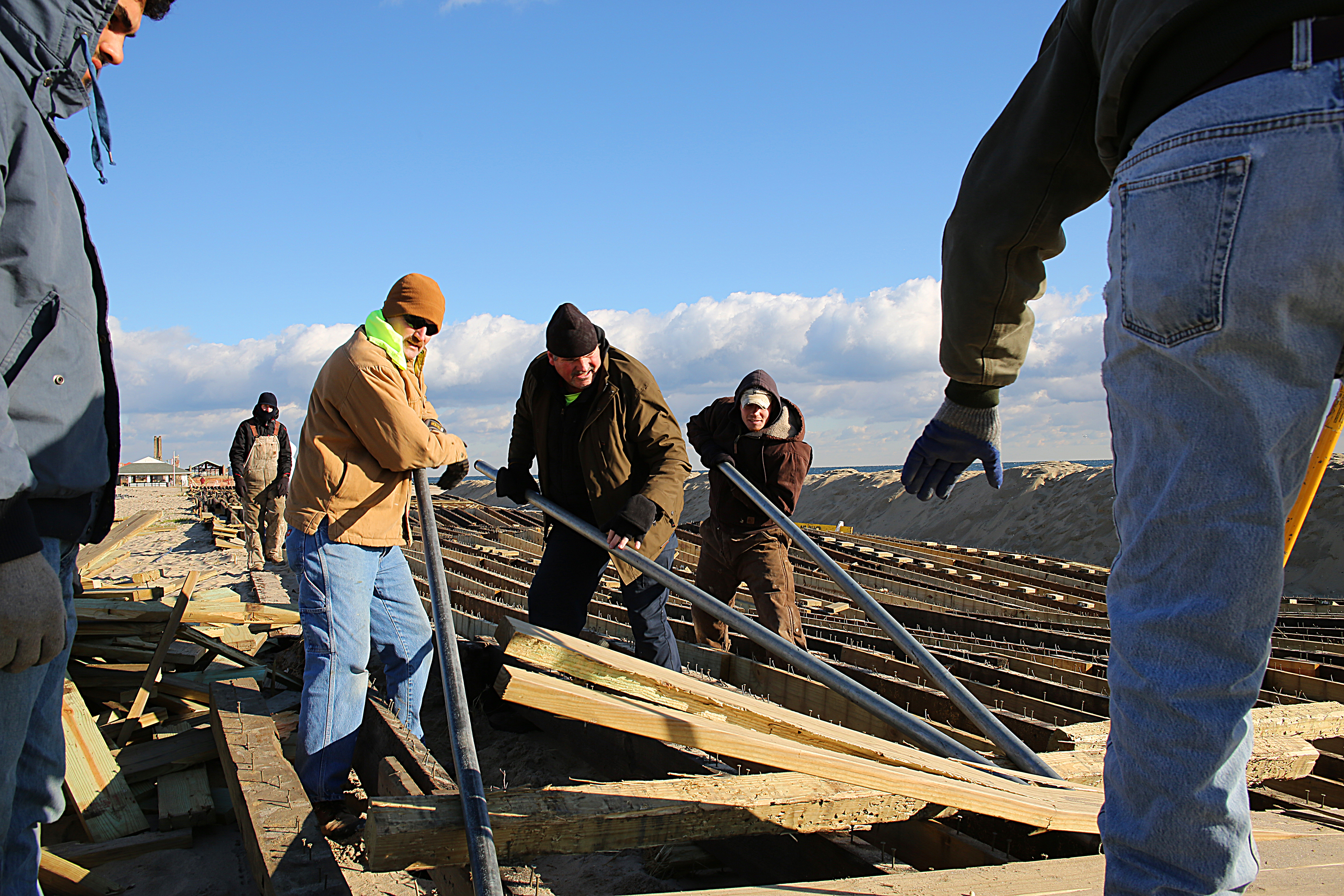 Workers in winter clothing handle wooden planks and debris at a storm-damaged structure.