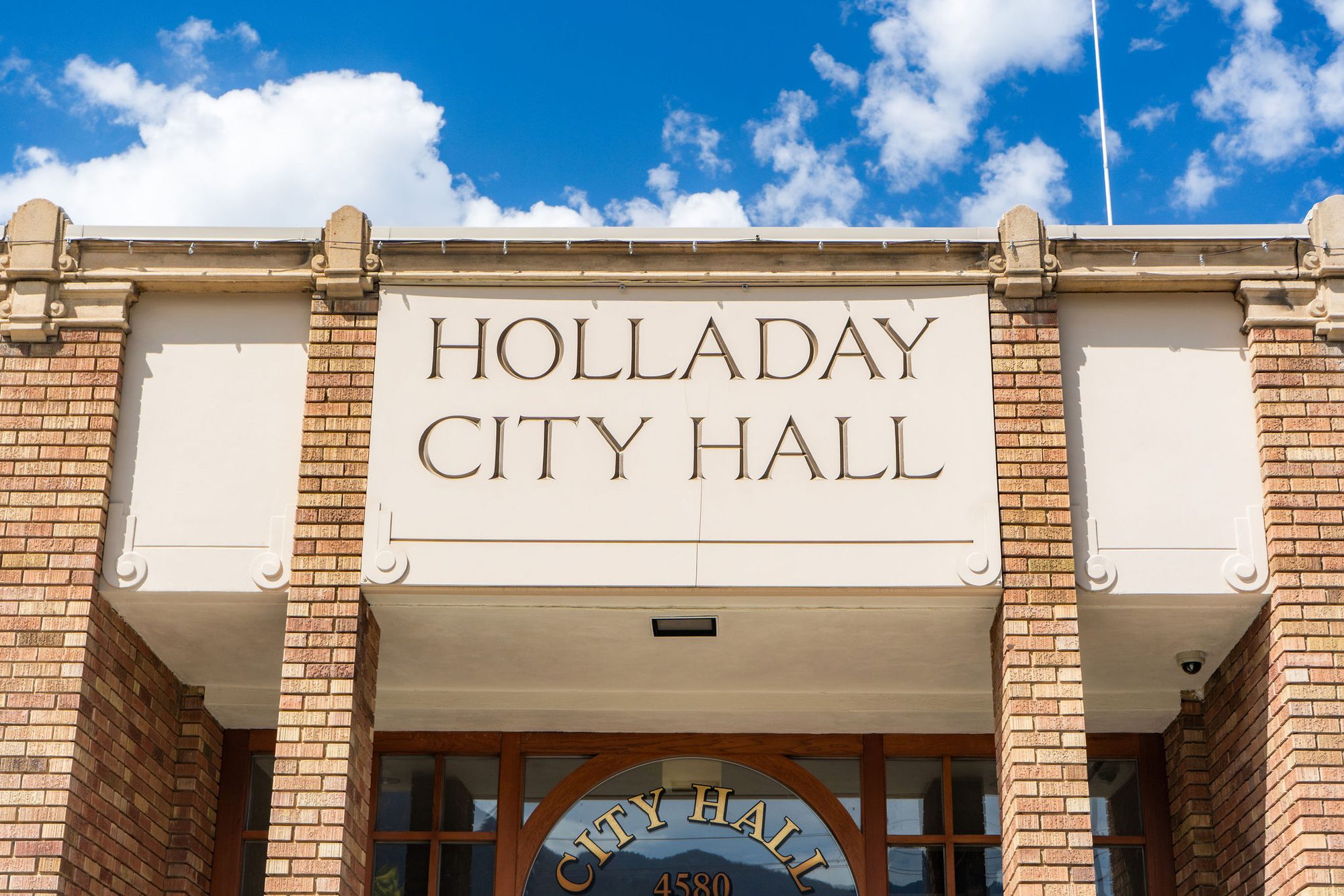 Exterior sign reading Holladay City Hall on a brick building facade under blue sky