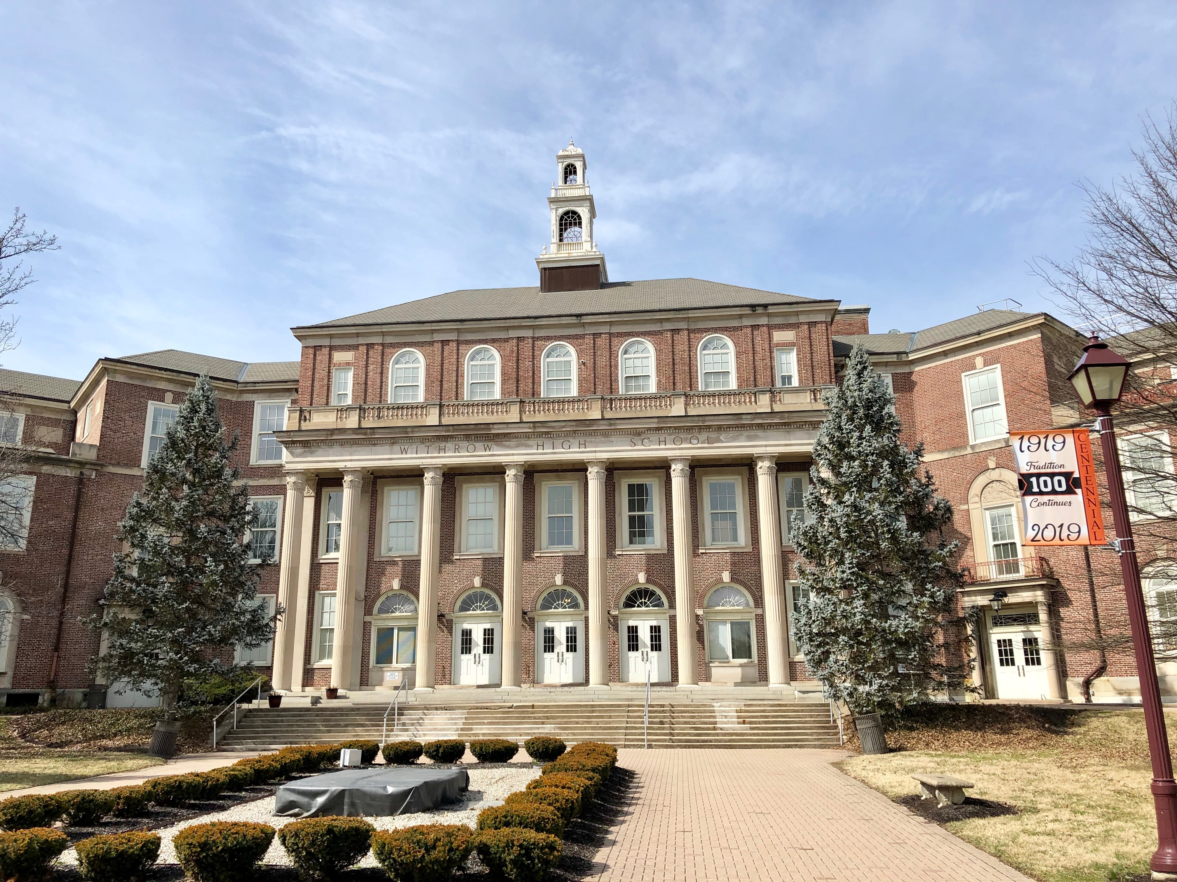 Large brick school building with white columns, a bell tower, and a centennial banner.