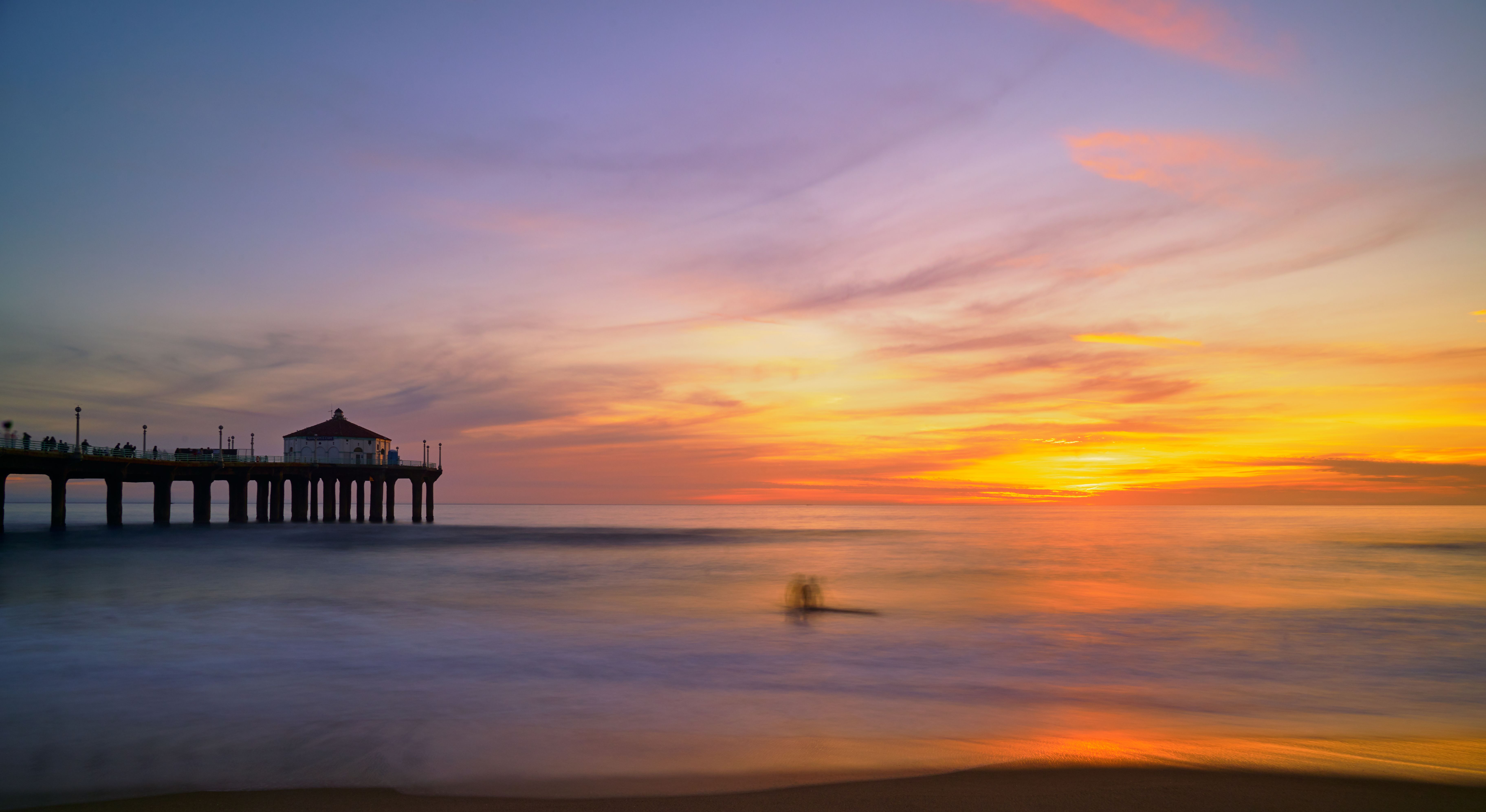 A pier pavilion silhouetted against a vivid orange and pink sunset sky over calm ocean water.