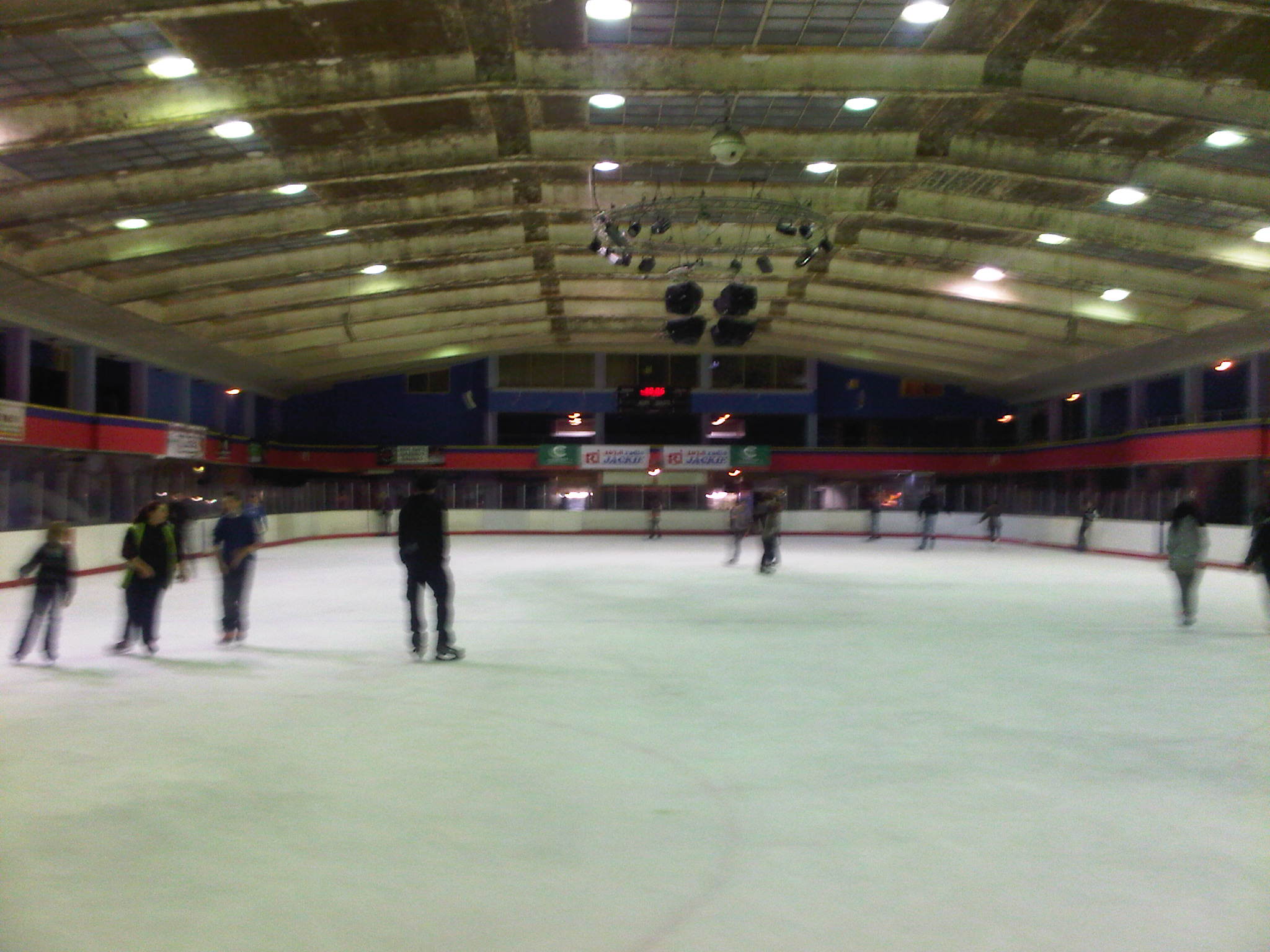Multiple skaters on an indoor ice rink with overhead lighting.