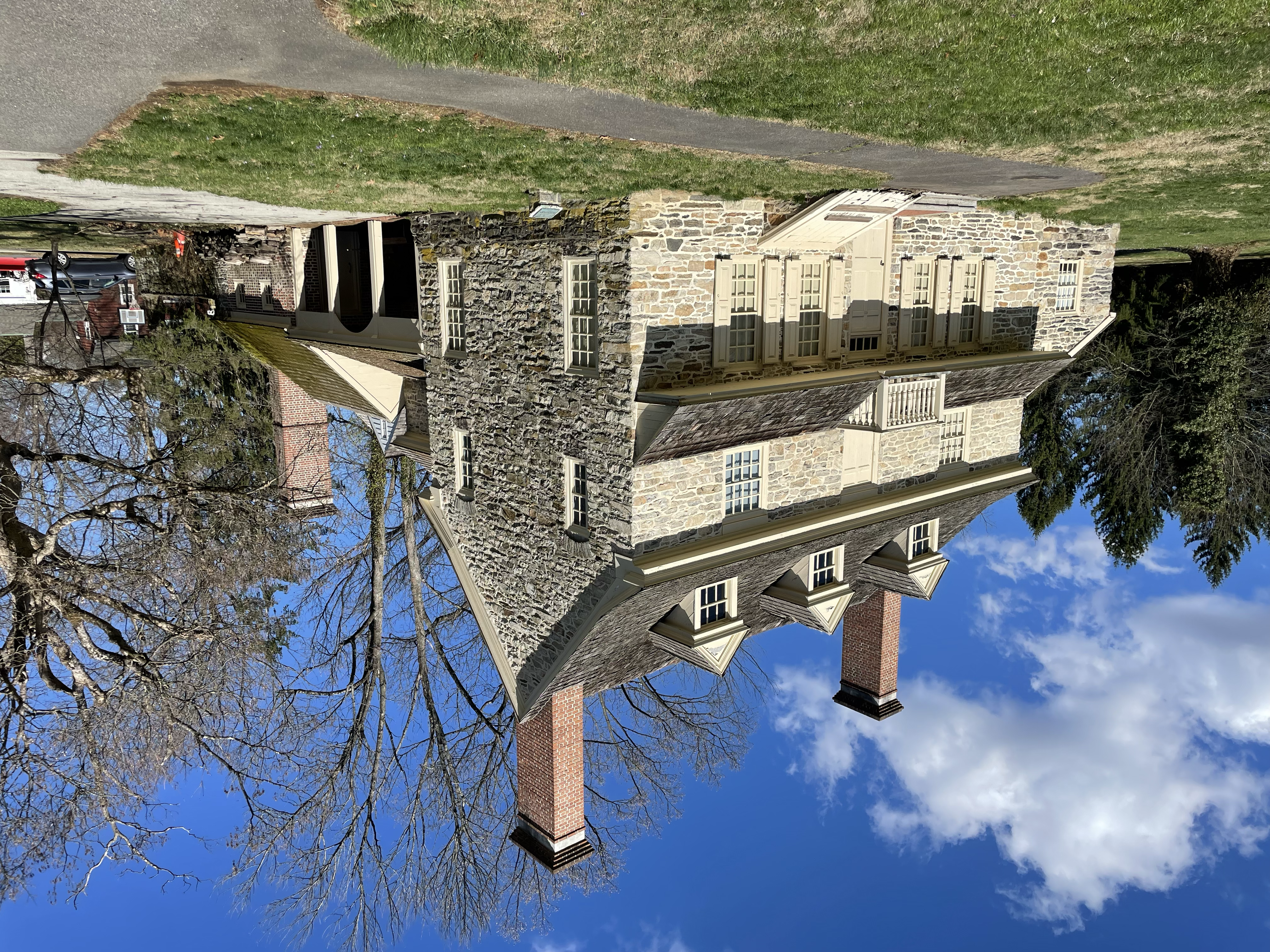 Front exterior of a two-story historic stone farmhouse with dormer windows and brick chimneys.