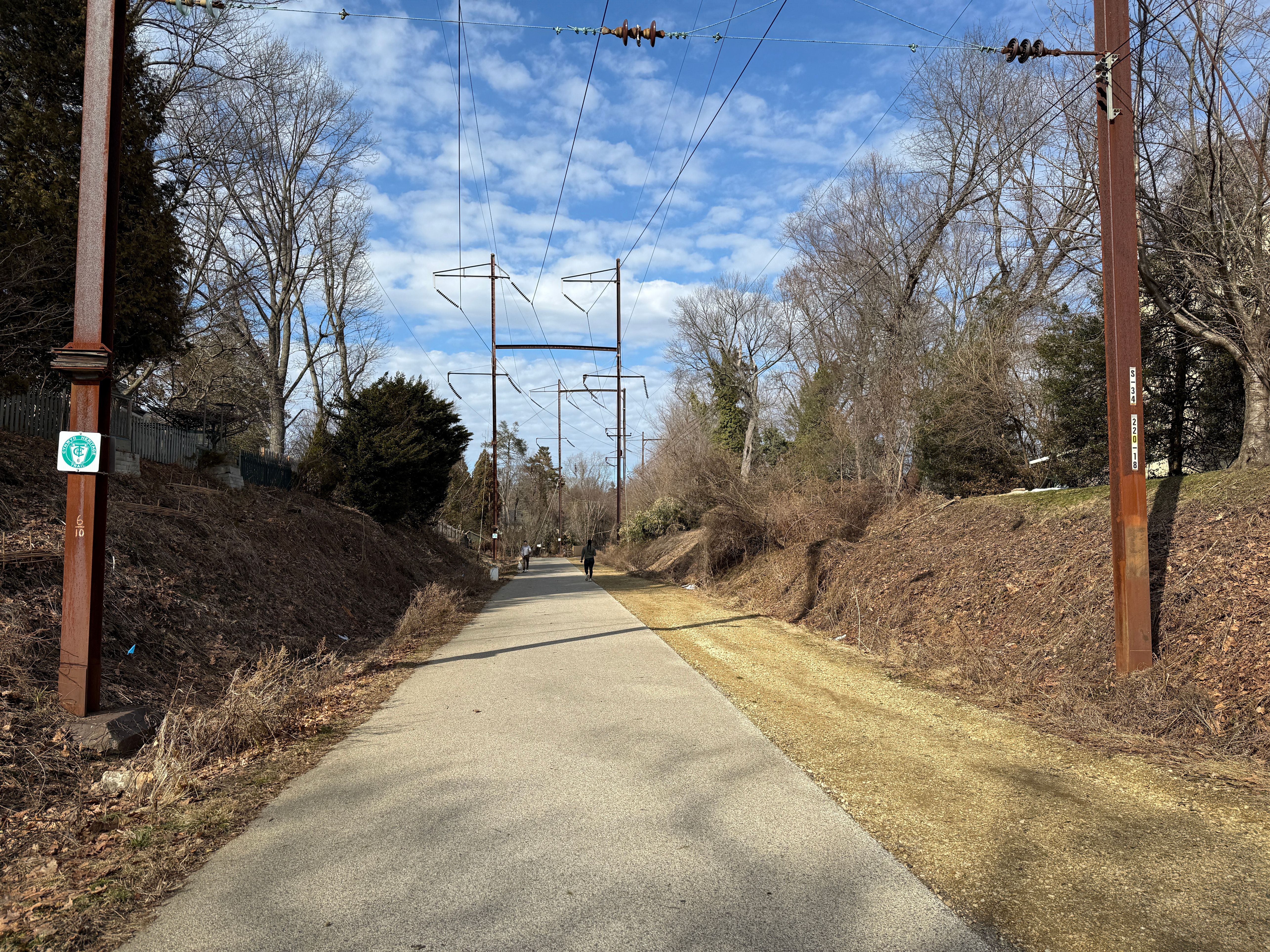 Paved trail stretching into the distance between earthen embankments and bare trees.