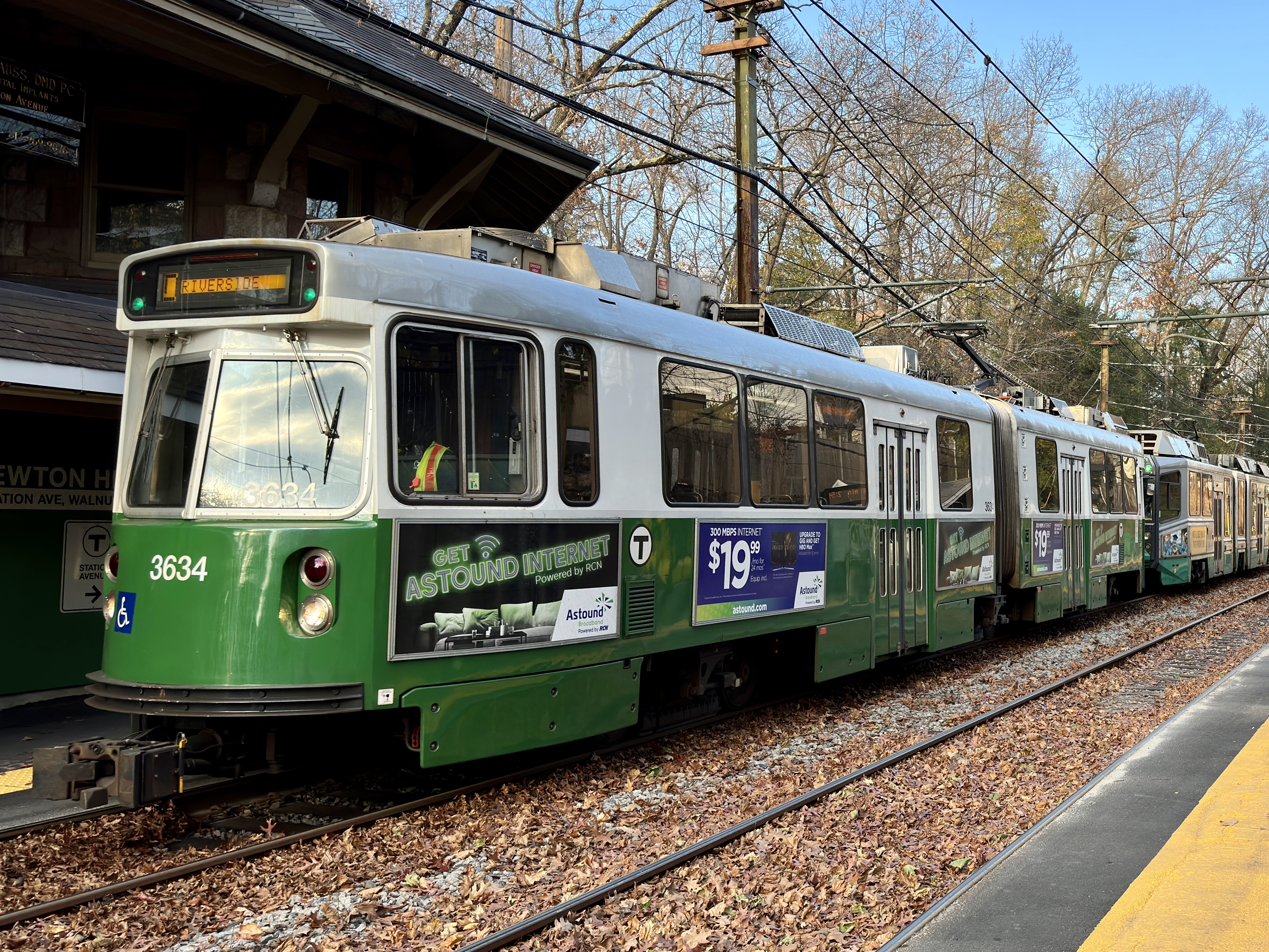 Green MBTA train at Newton Highlands station platform, historic wooden shelter visible behind.