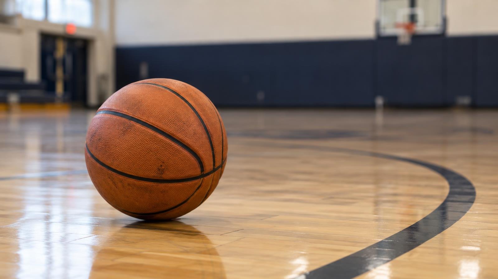 Orange basketball resting on a hardwood gymnasium floor near the three-point arc.