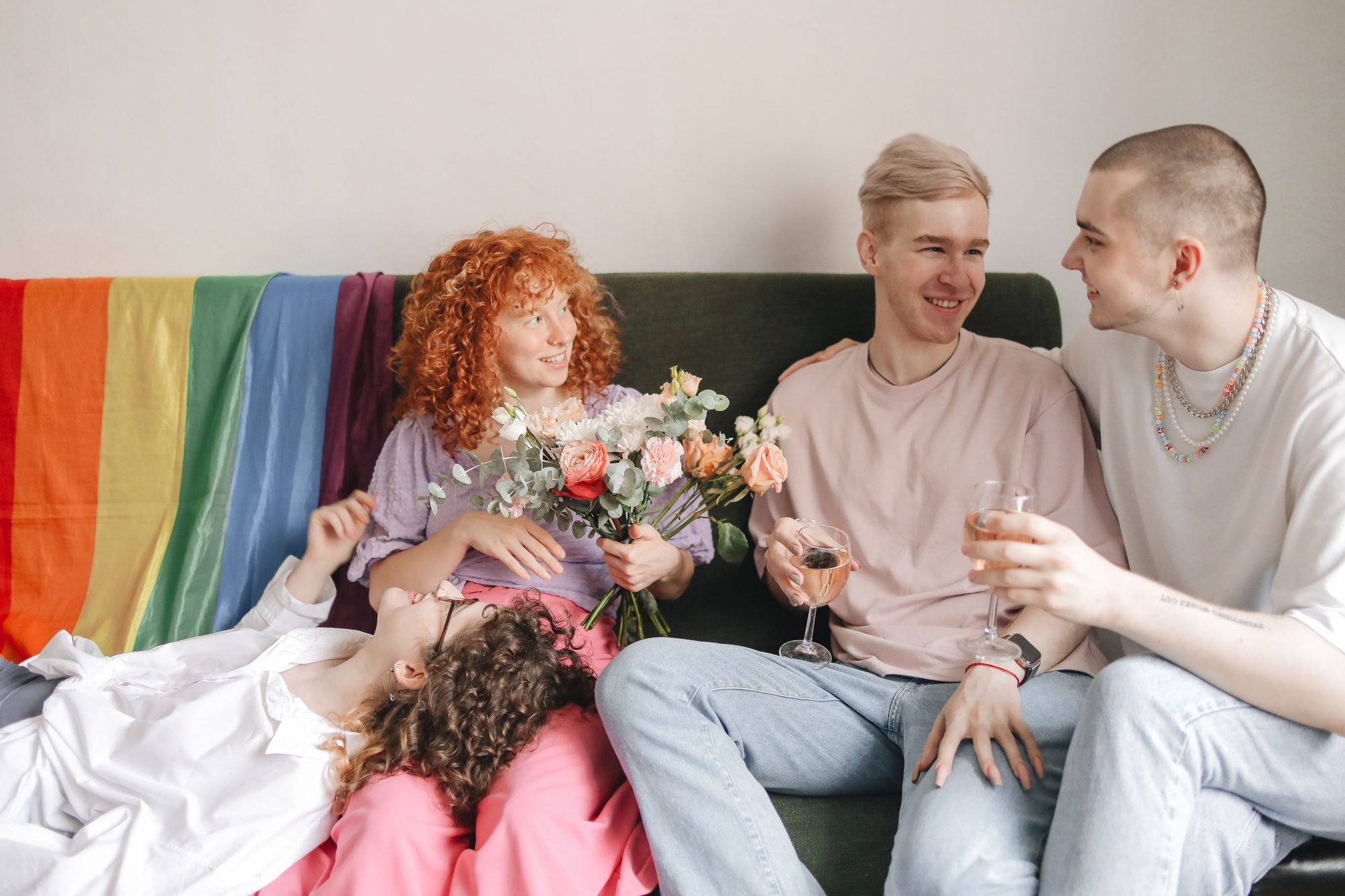 Group of young LGBTQ adults enjoying a friendly indoor gathering with wine and flowers.