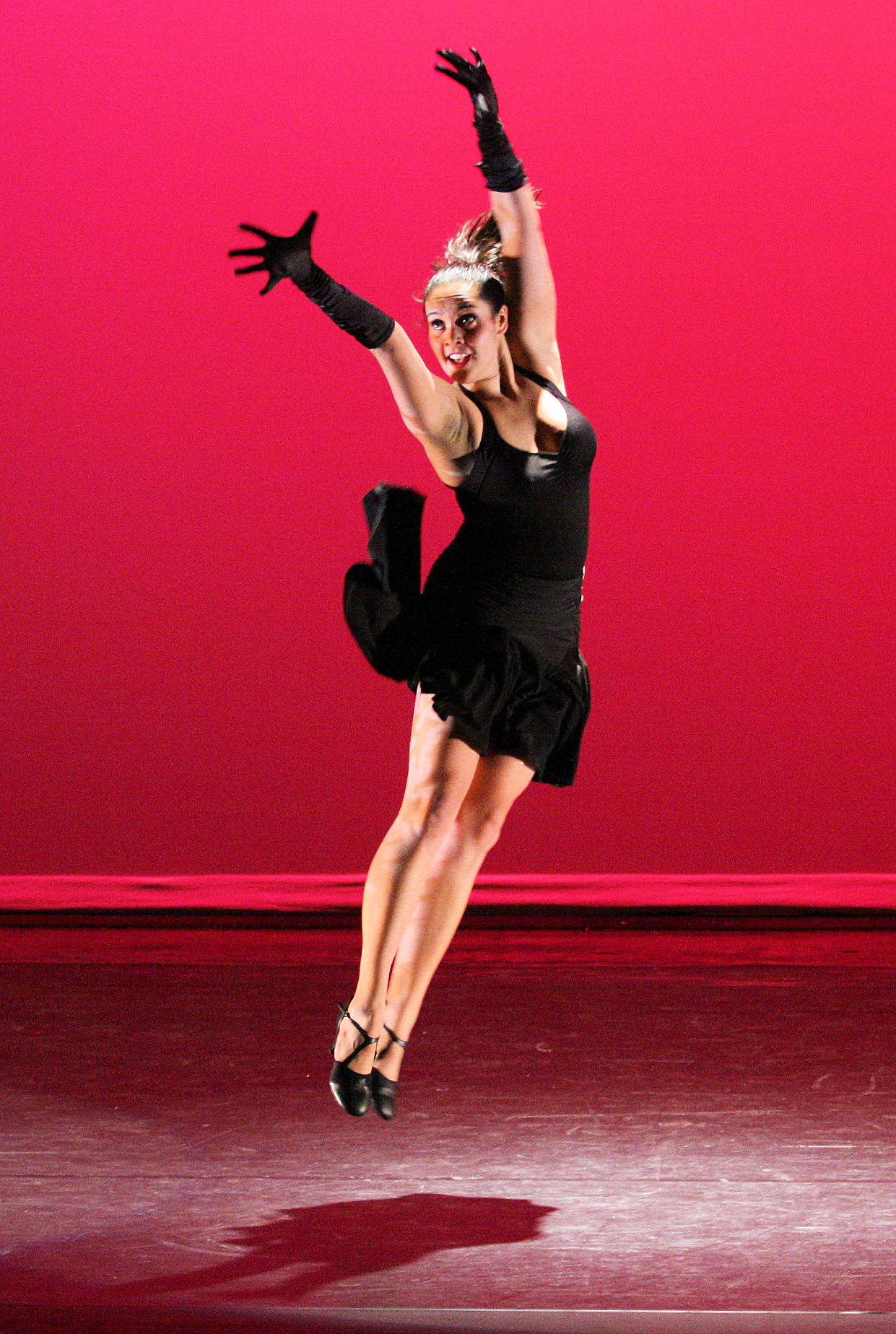 A tap dancer leaps mid-air during a stage performance against a red backdrop.