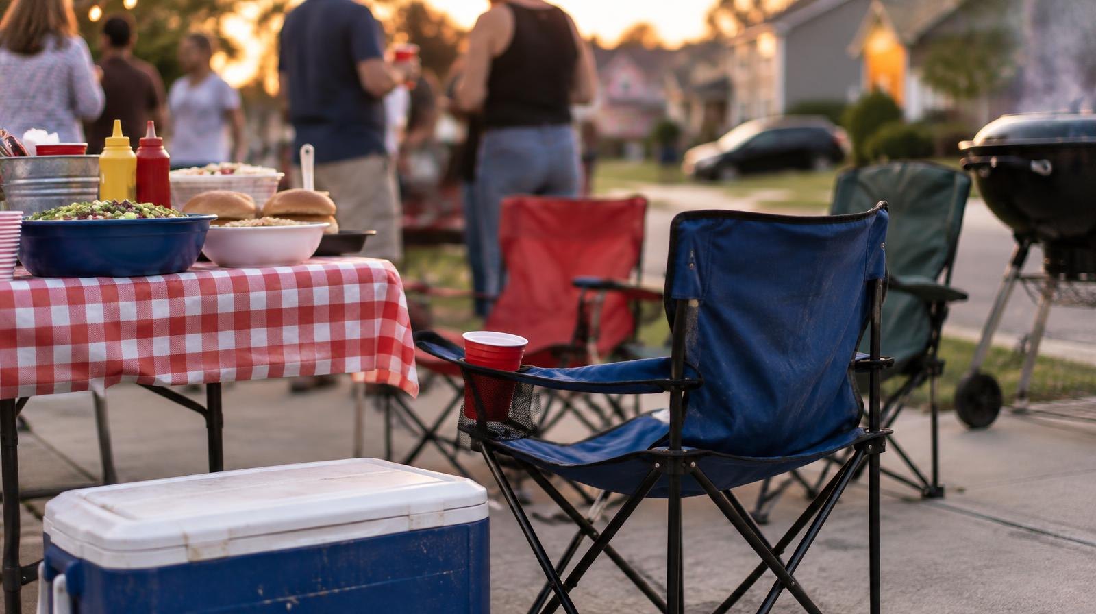 Folding chairs and a cooler arranged on a residential driveway at dusk.