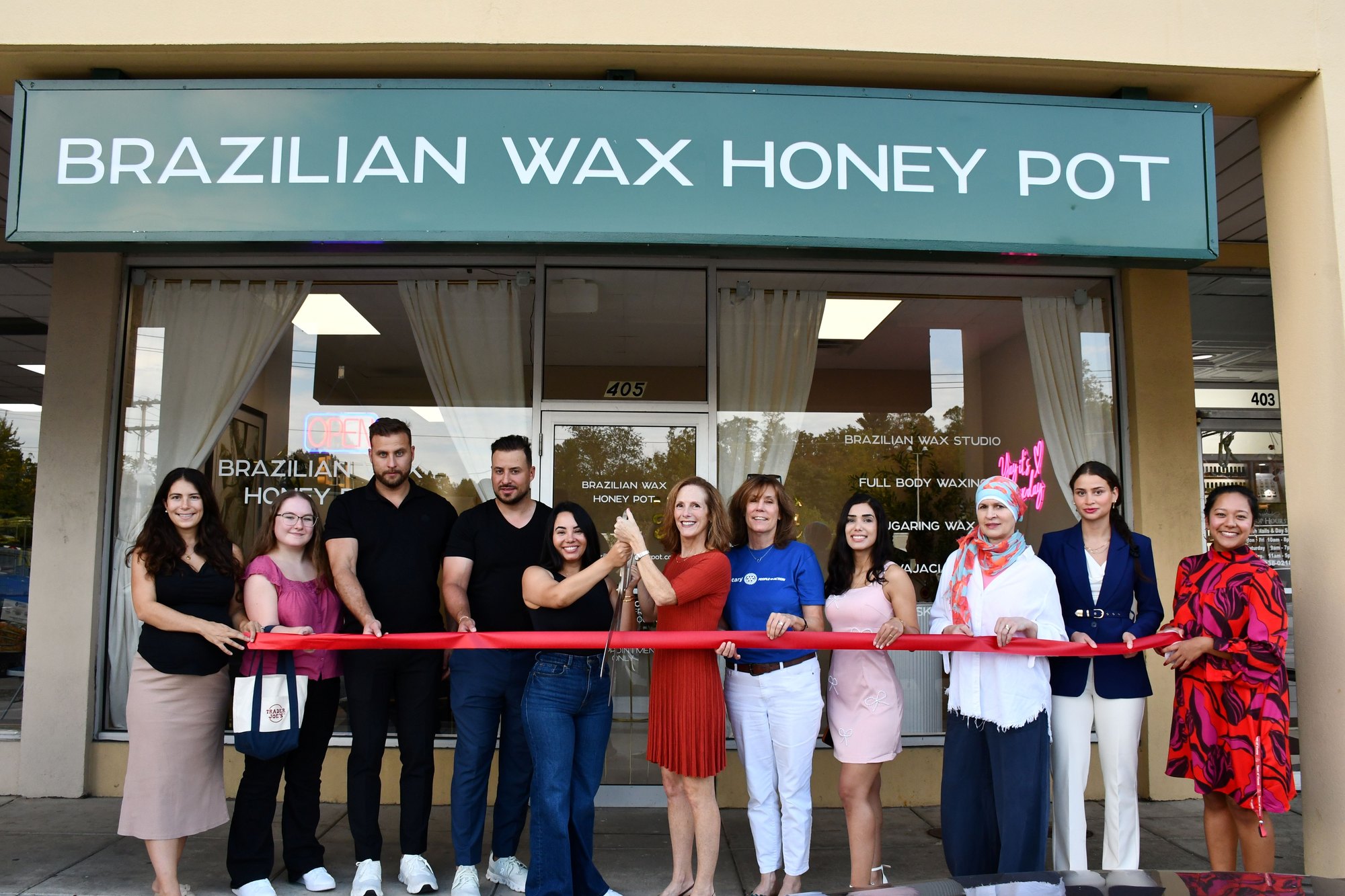 A group of people hold a red ribbon in front of a waxing studio storefront.