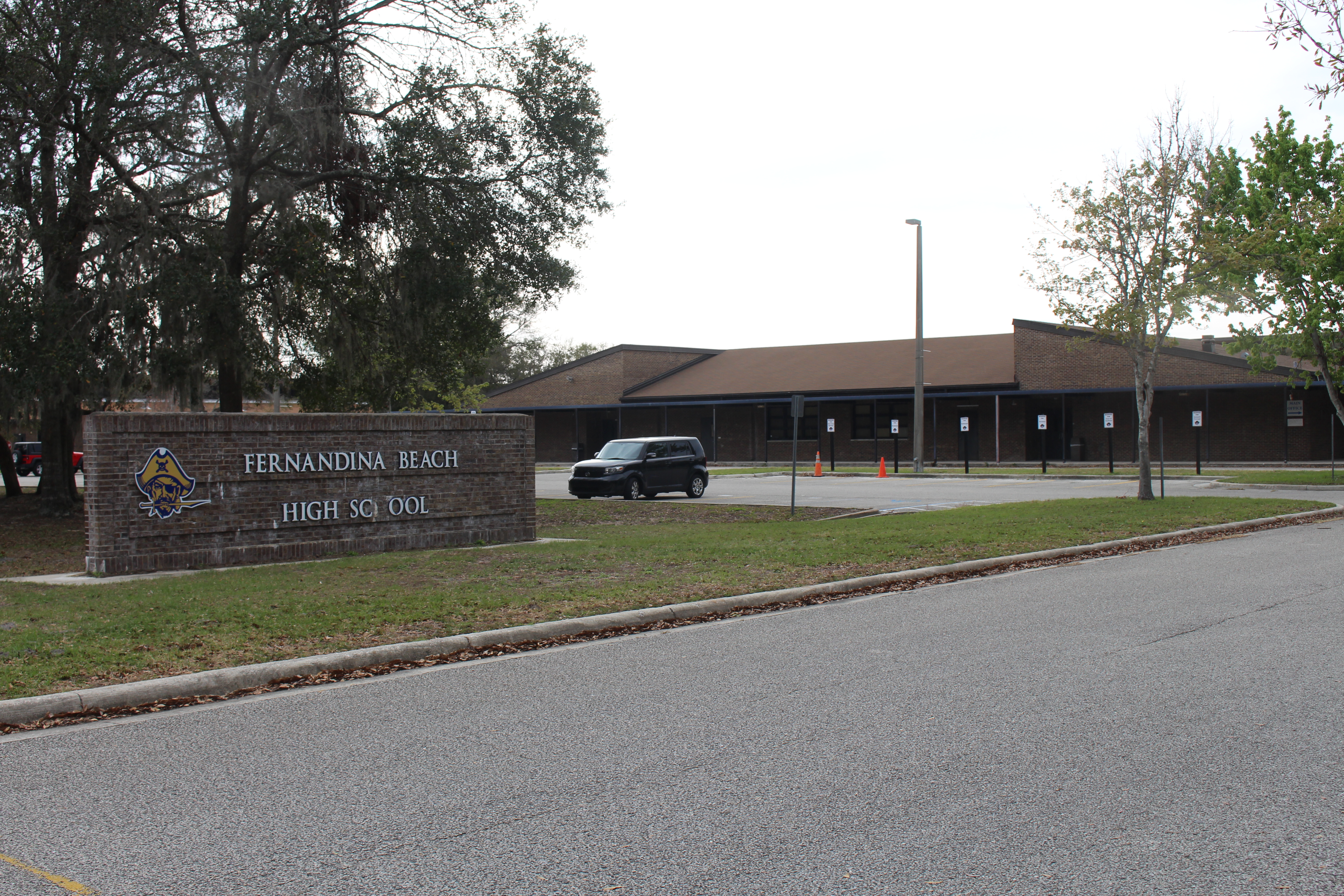 Brick entrance sign and exterior of a single-story school building surrounded by trees.