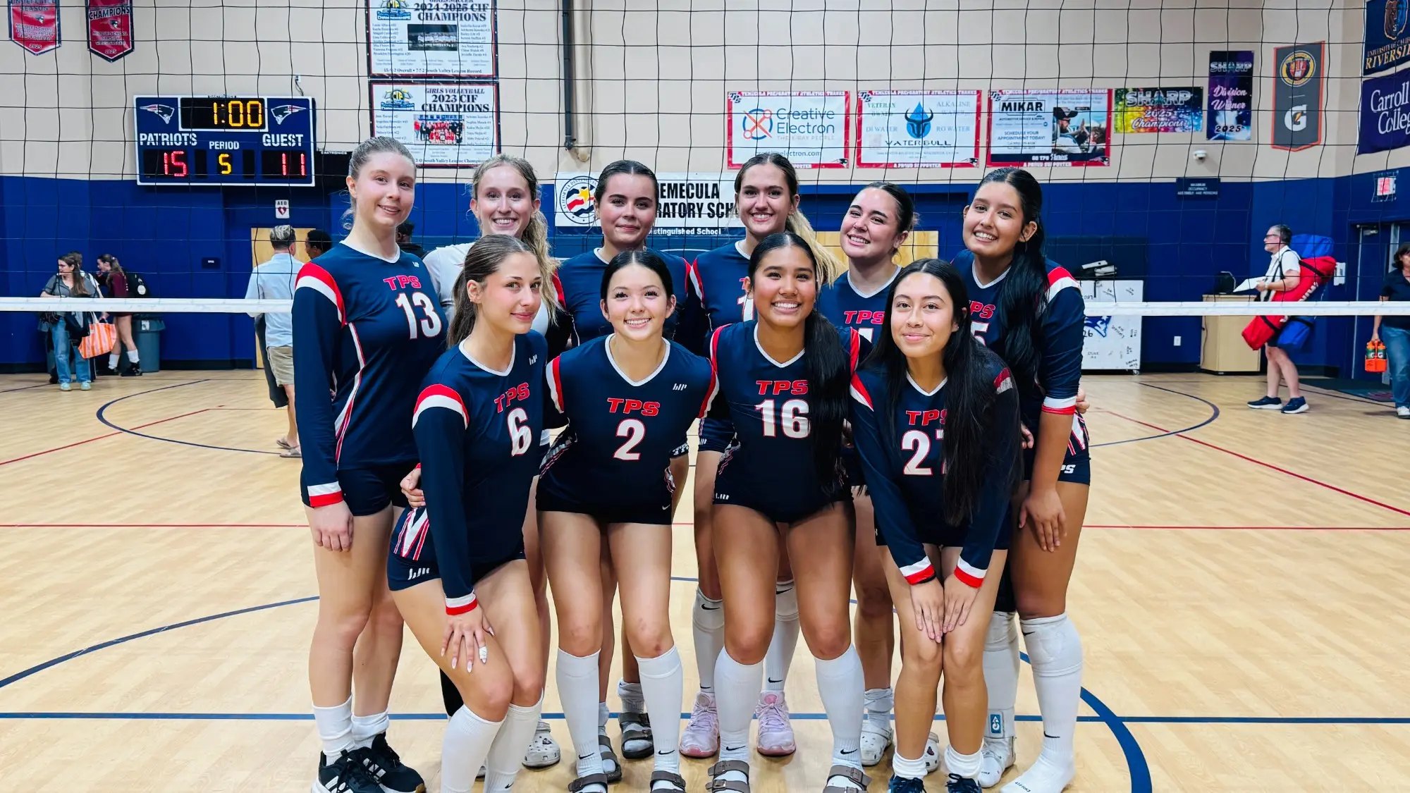 Girls volleyball team in navy uniforms poses together in a gymnasium.