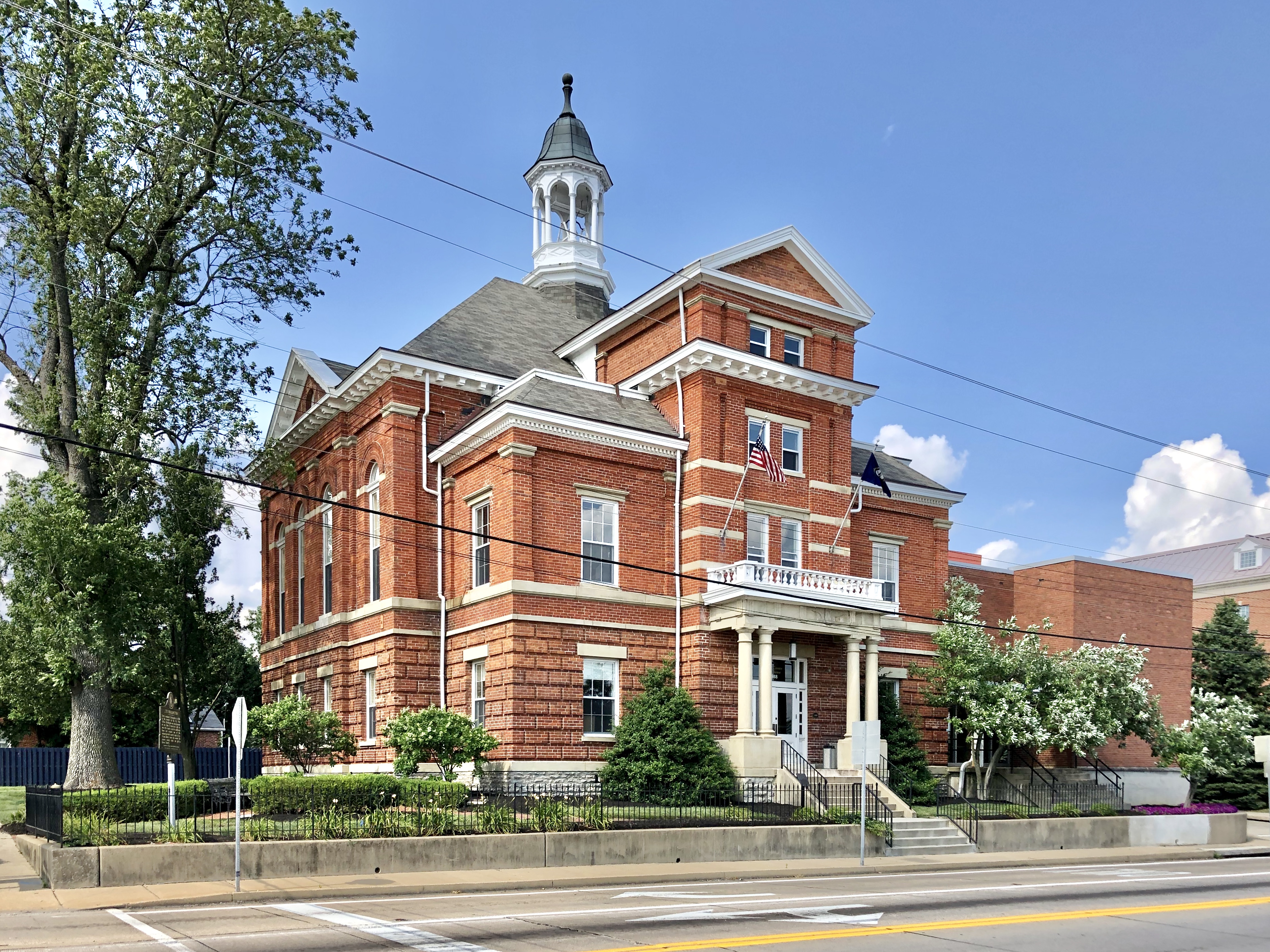Red brick courthouse with white cupola, columns, and American flag on a sunny day.