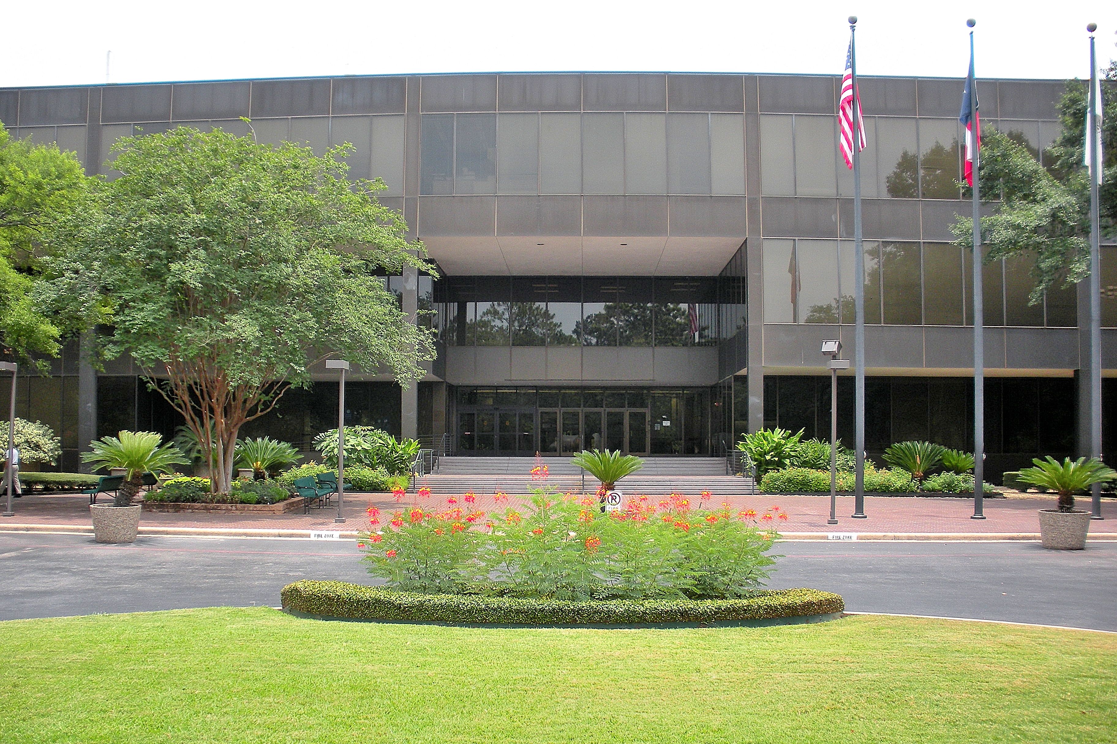 Glass and concrete university building with flagpoles and a circular garden.