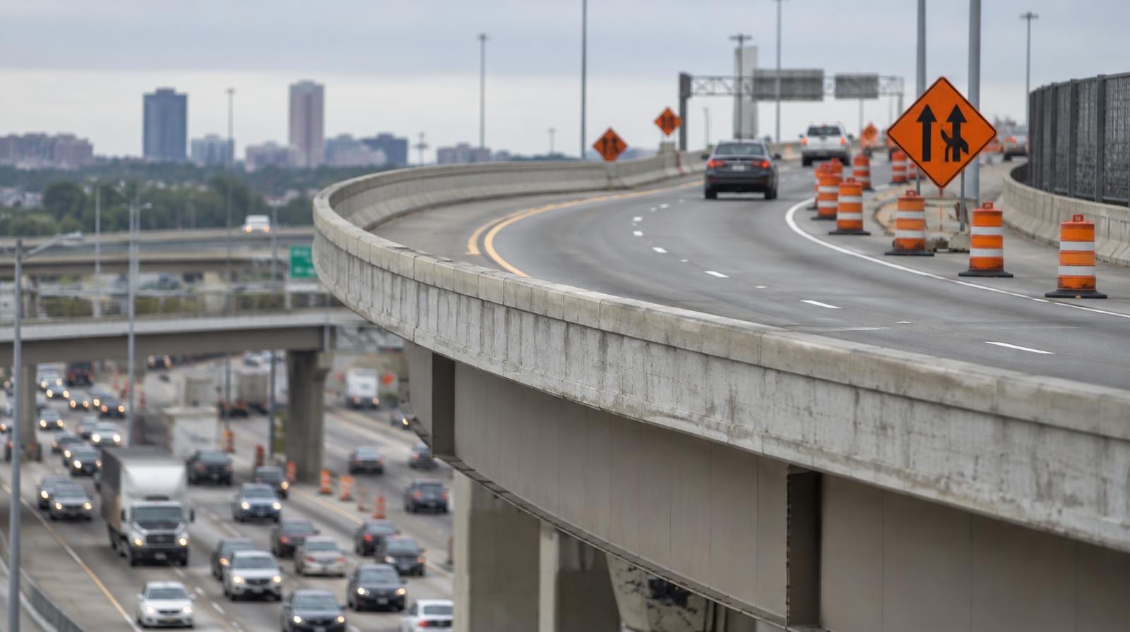 Elevated freeway HOV ramp curving over a highway interchange with orange construction barrels.