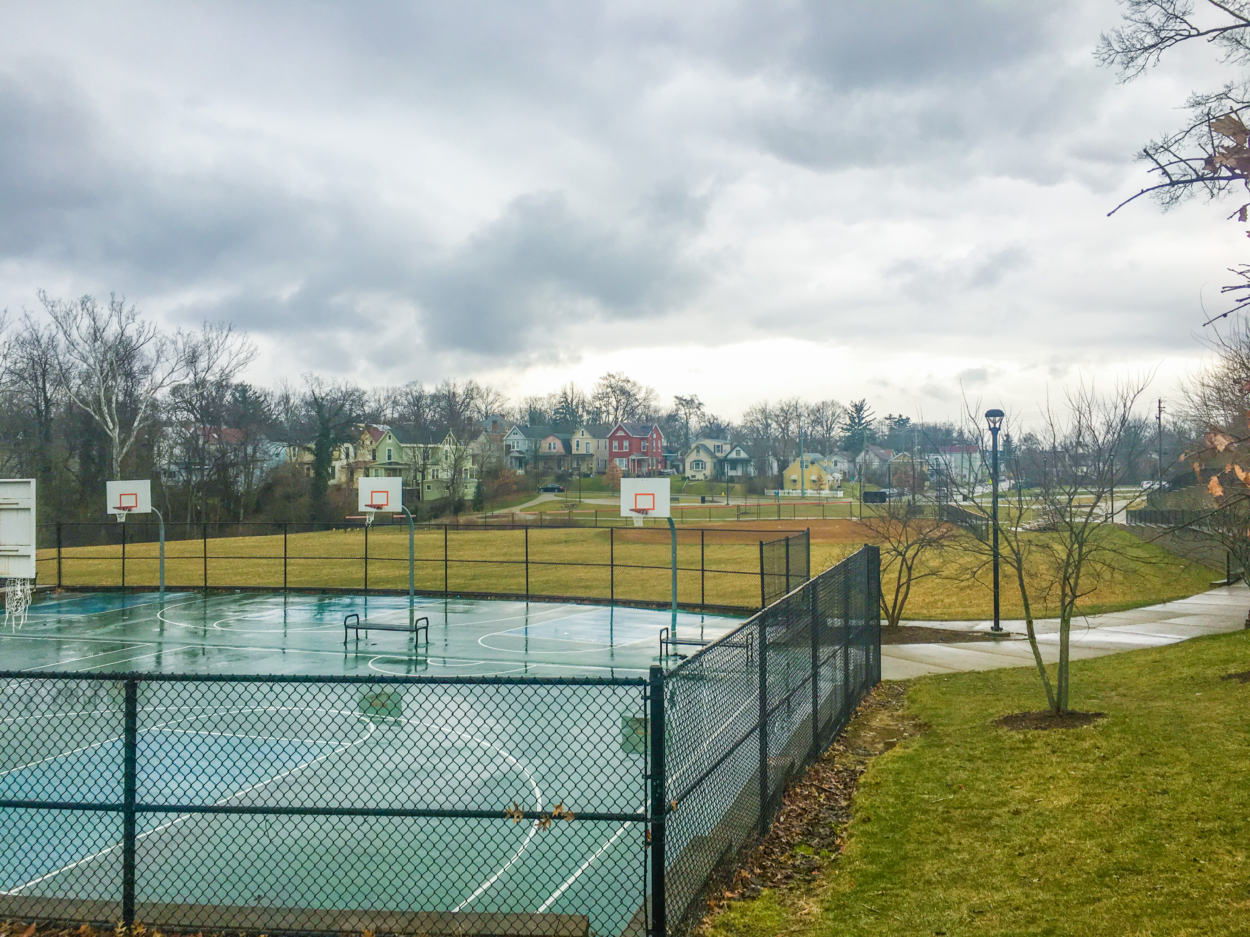 Fenced basketball courts and open grass fields at an urban neighborhood park.
