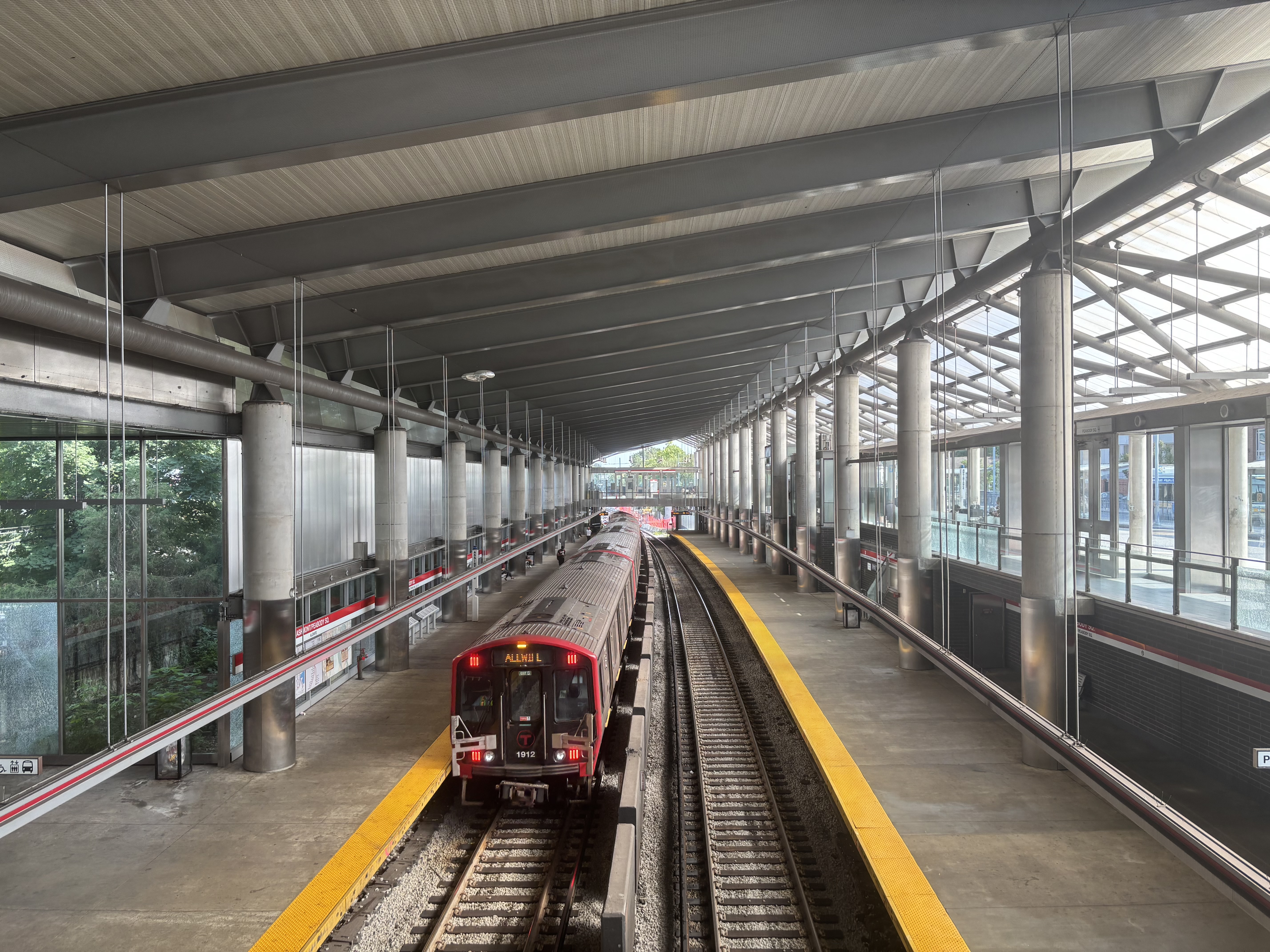 A red MBTA subway train arrives at a covered station platform.