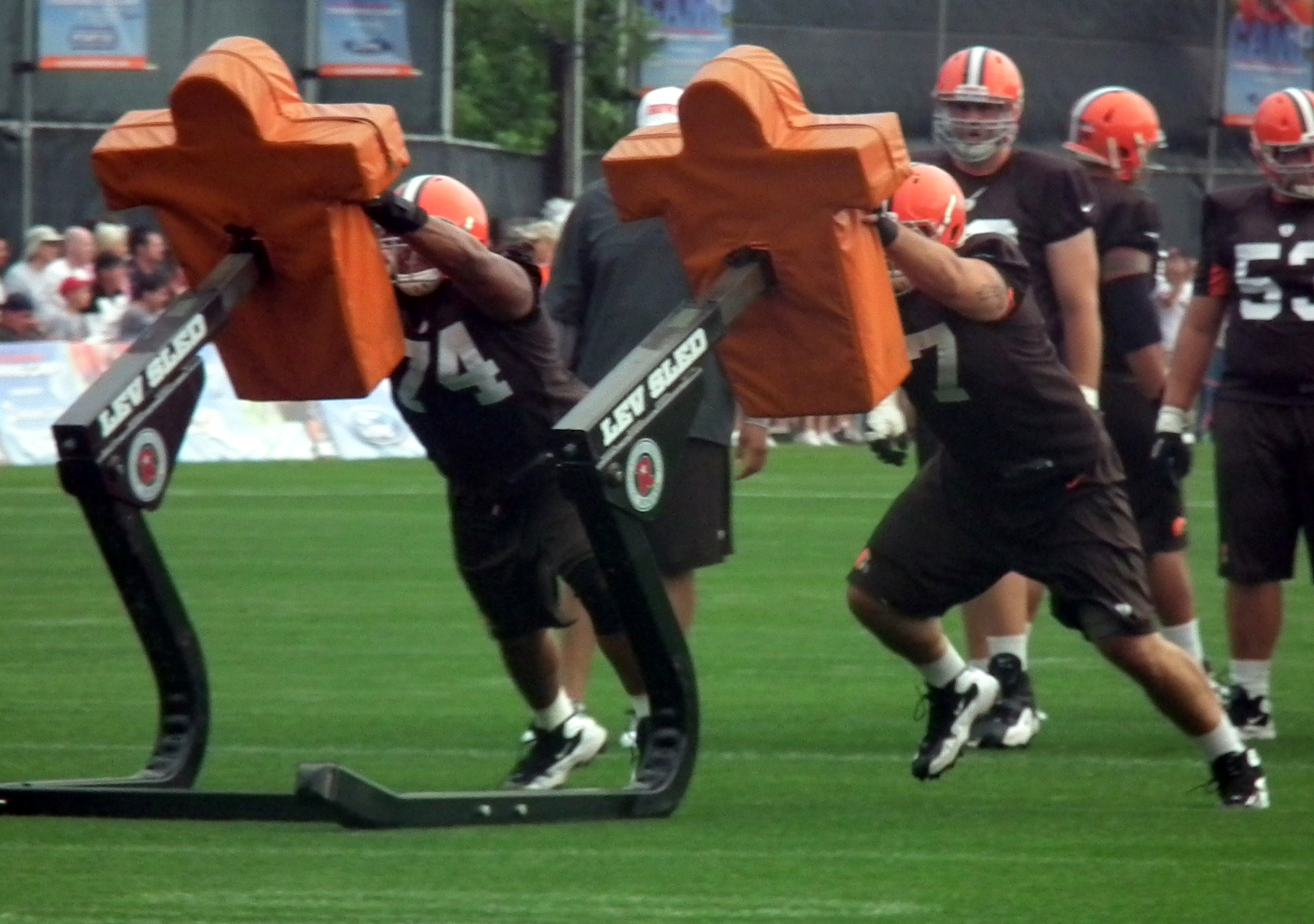 Football players in uniform drive into padded blocking sleds during a practice drill.