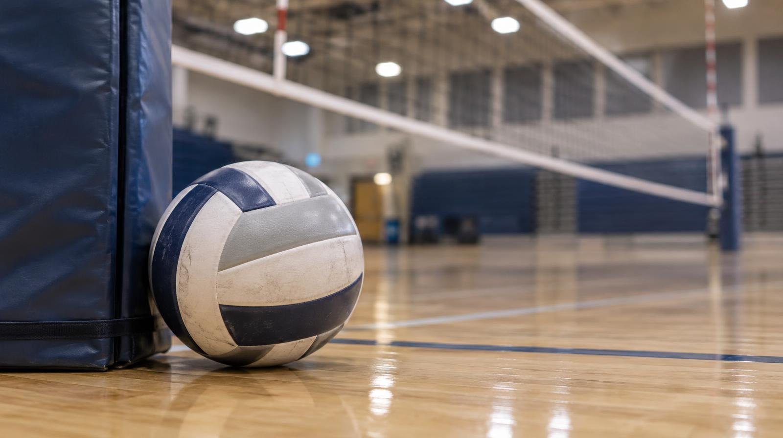 A volleyball resting on a gymnasium floor next to a net post.