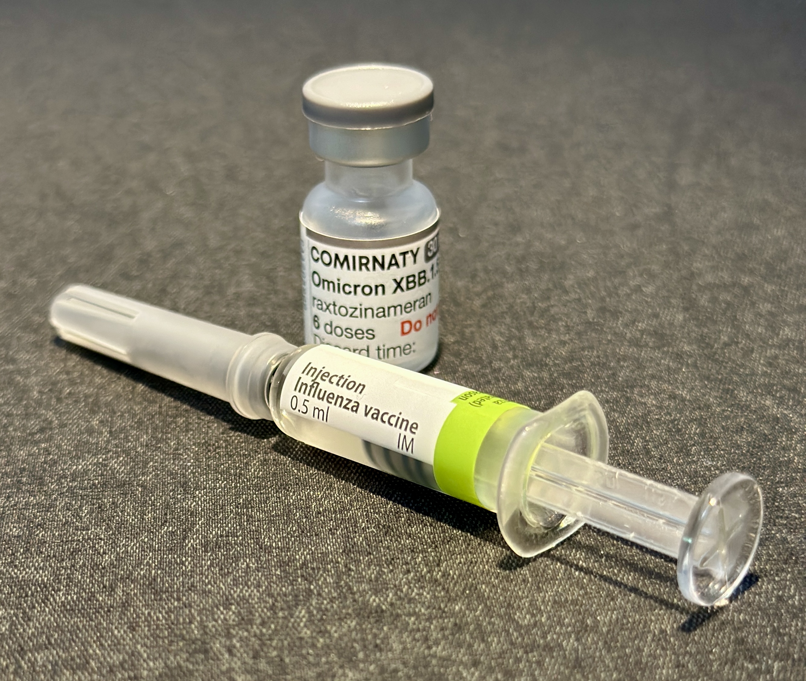 Vaccine vial and pre-filled flu shot syringe resting on a gray surface.