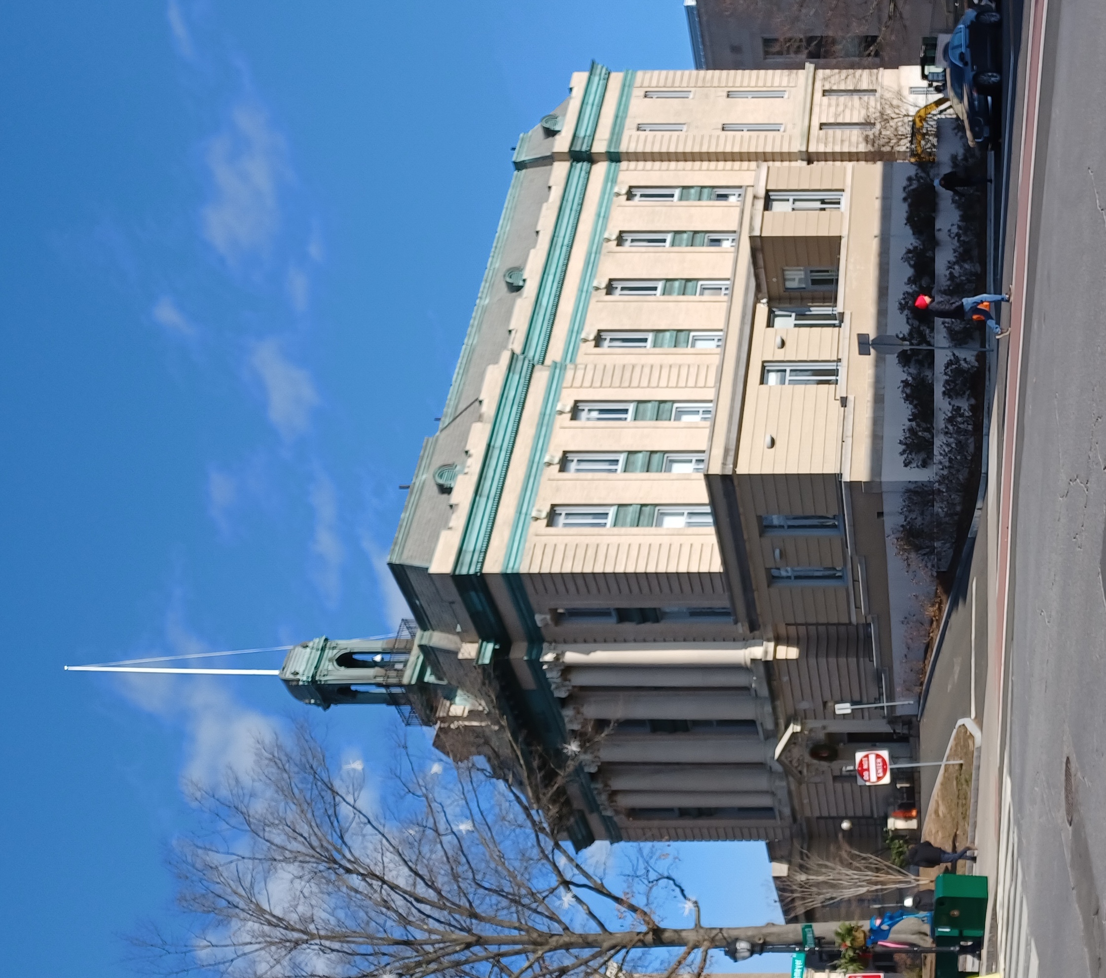 Neoclassical civic building with tall columns, green copper roof, and spire against a blue sky.