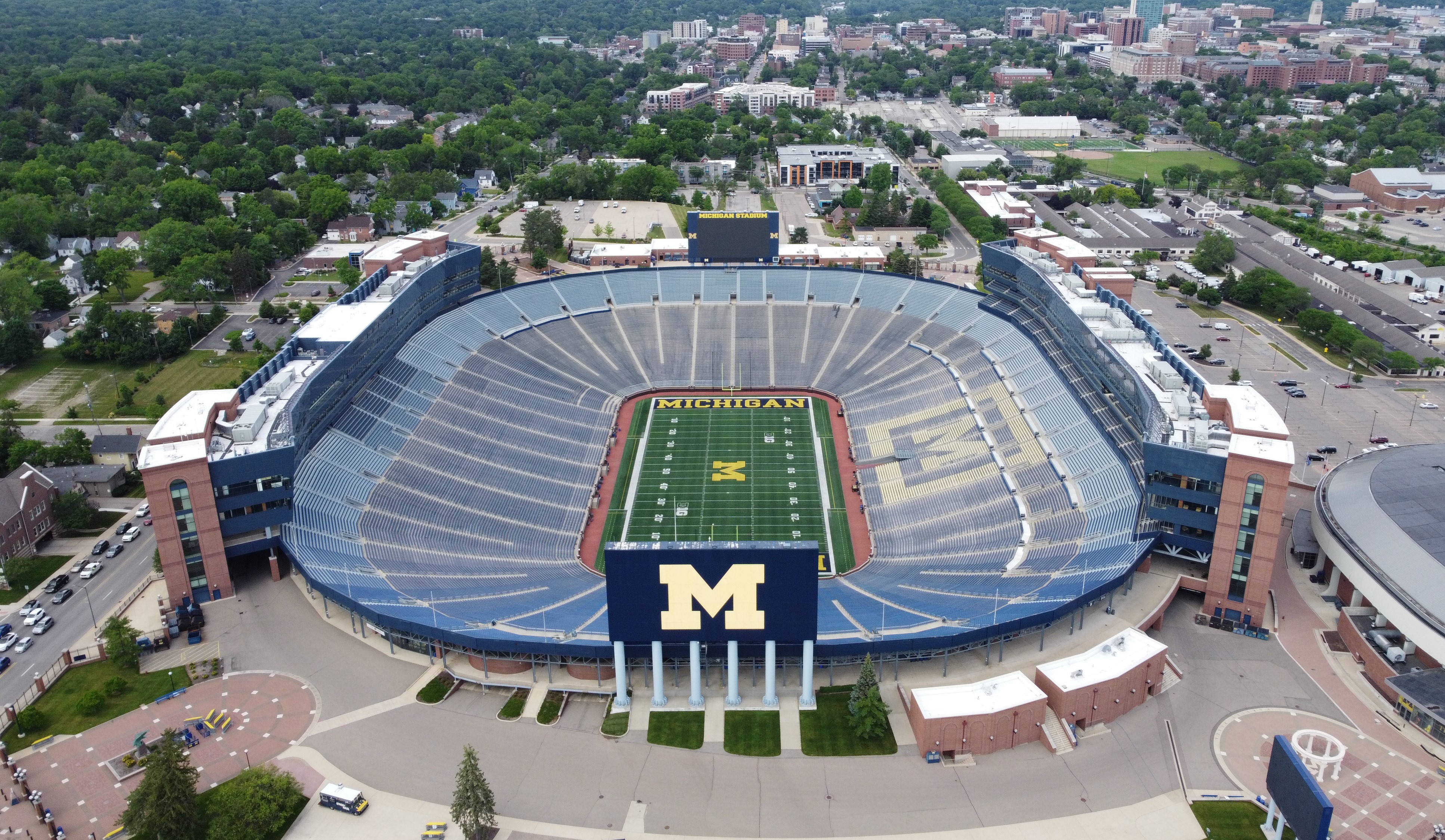 Aerial view of a large open-air football stadium with a block M logo at midfield.