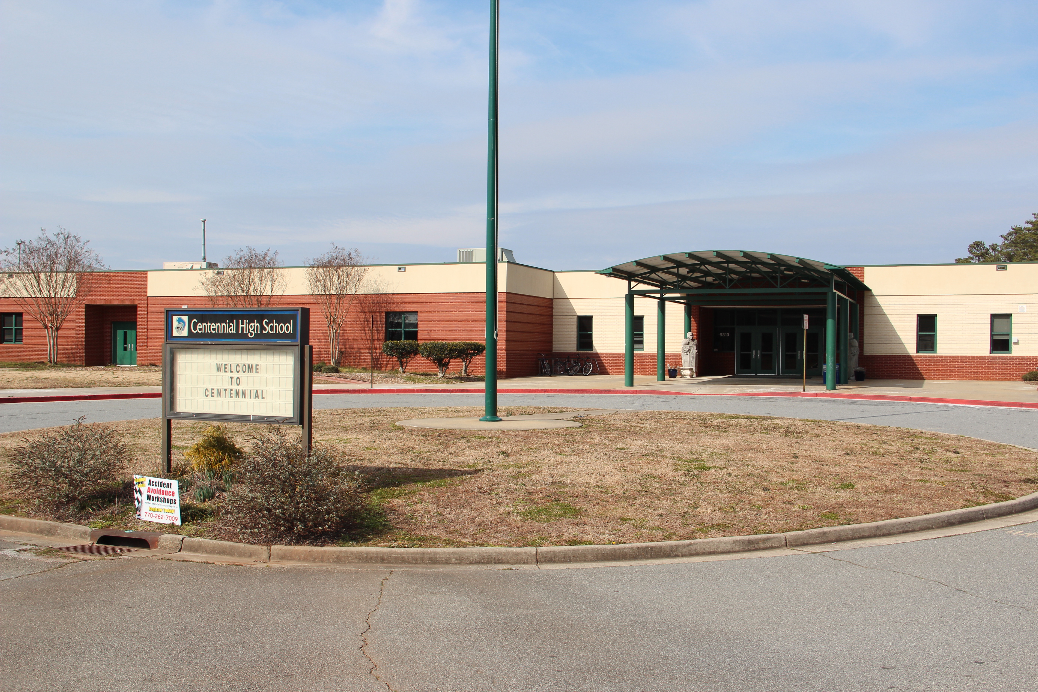 School entrance with green canopy and marquee sign reading Welcome to Centennial.