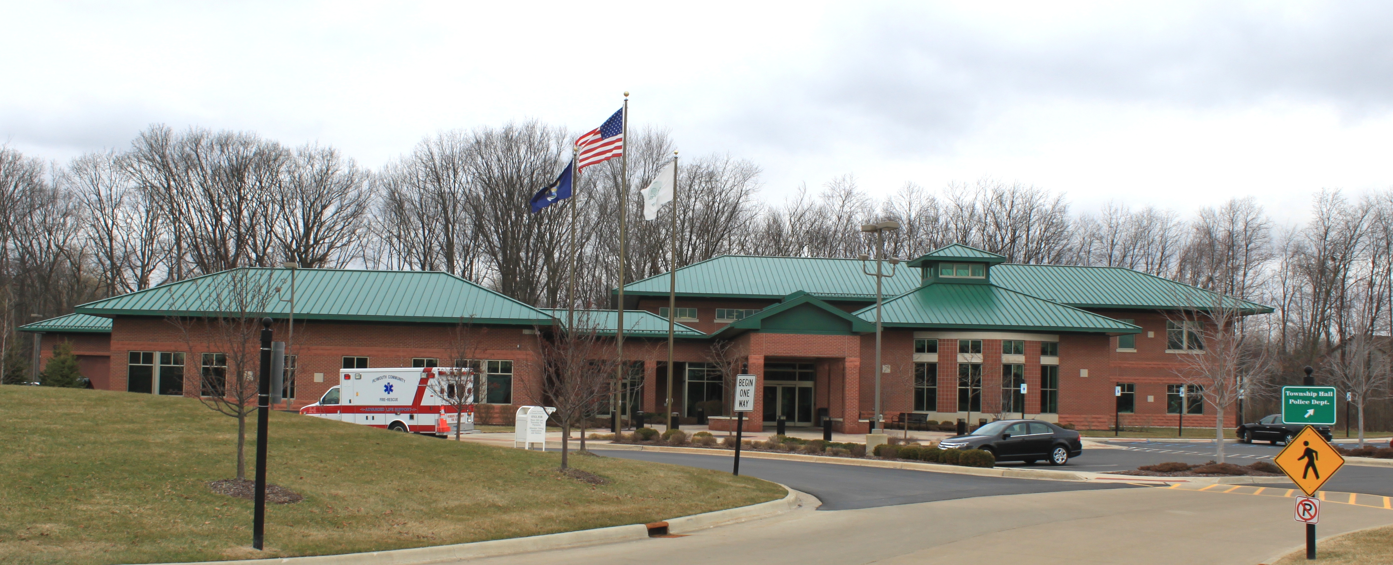 Brick municipal building with green metal roof and two flags on a flagpole.