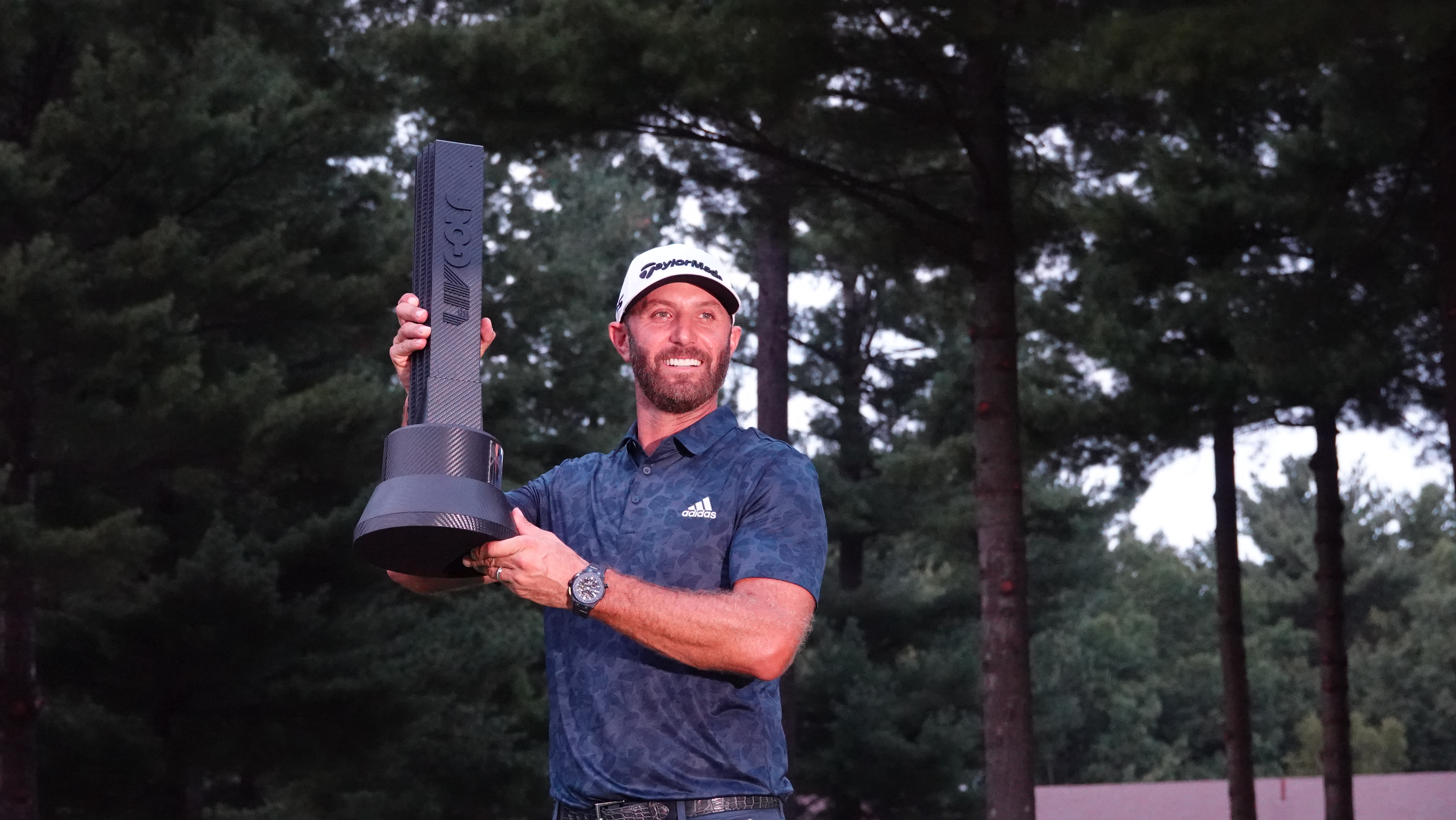 A golfer in an Adidas cap raises a large black LIV Golf championship trophy overhead.
