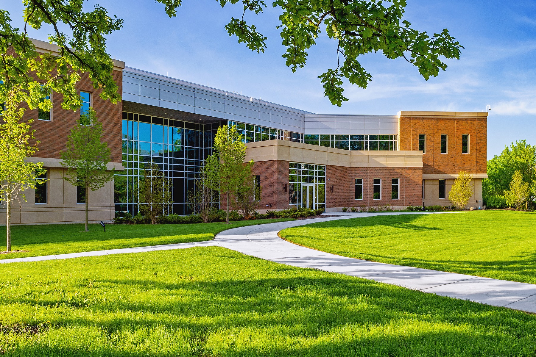Modern brick and glass academic building on a sunny campus with green lawns.