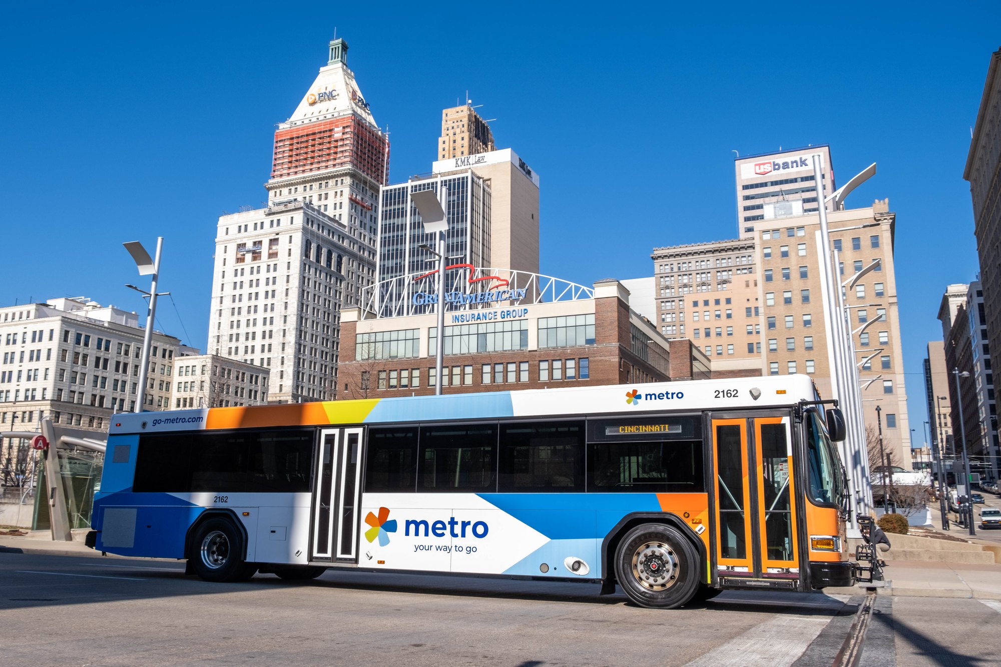 A Metro transit bus on a city street with Cincinnati skyscrapers in the background.