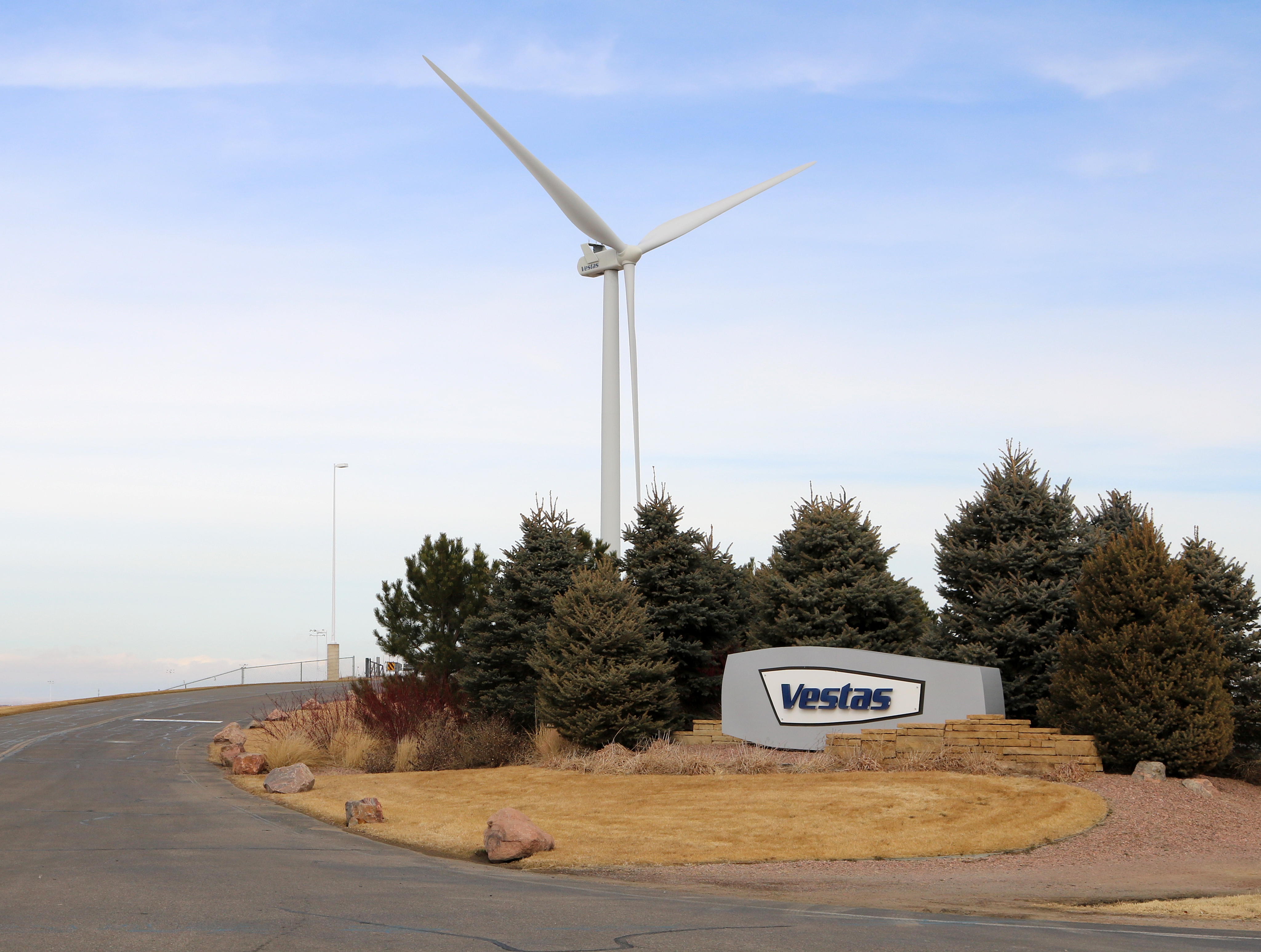 Stone entrance sign for Vestas Wind Systems with a wind turbine visible behind trees.