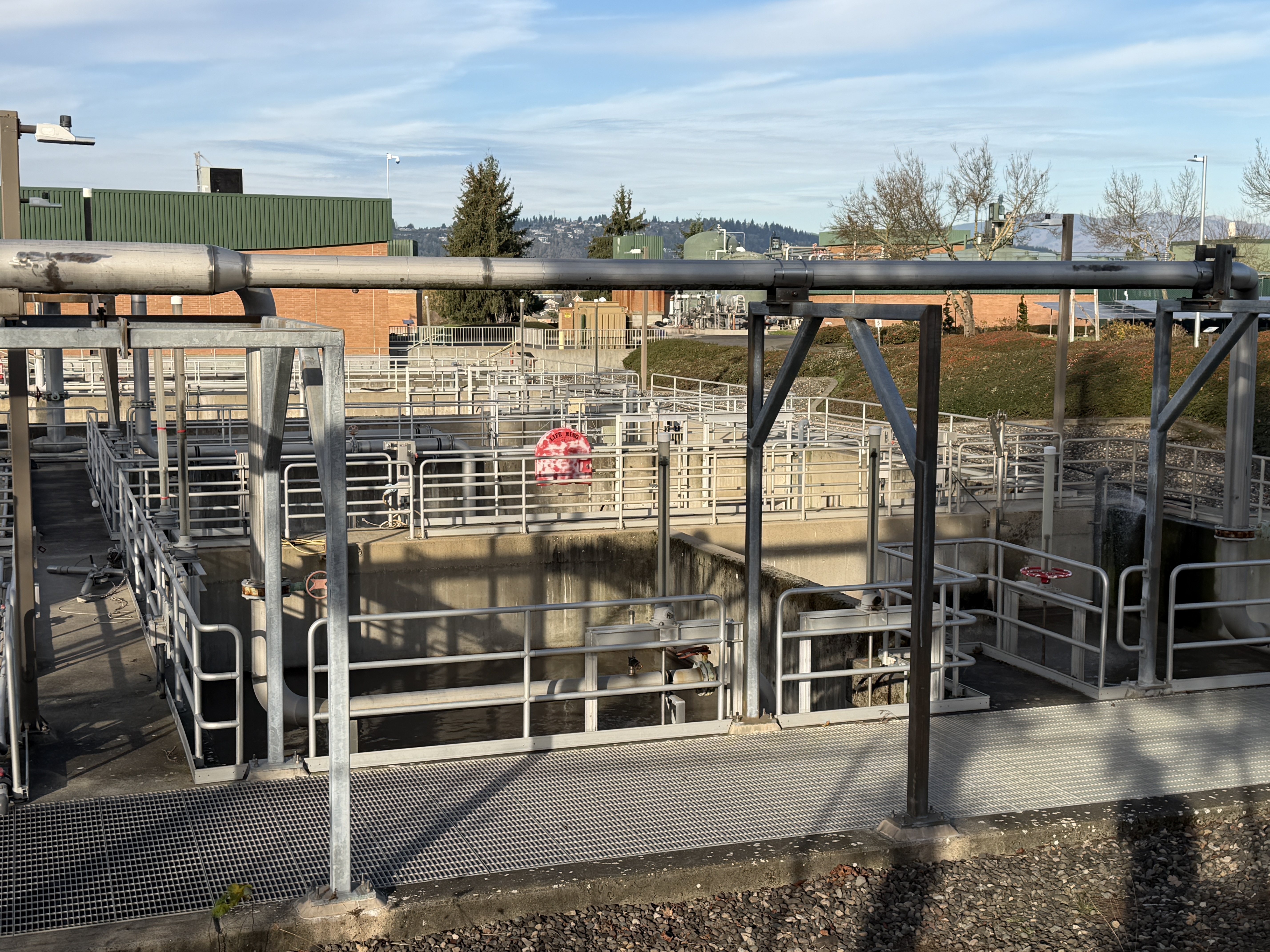 Circular clarifier tanks with metal walkways, railings, and large piping at a wastewater treatment plant.