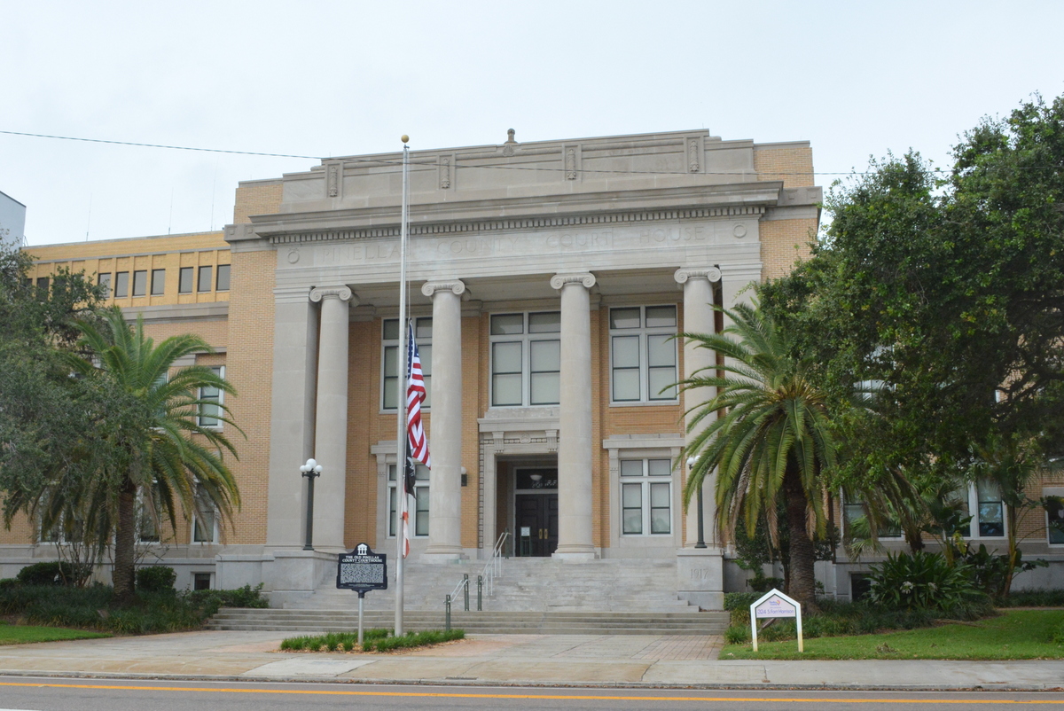 Neoclassical courthouse exterior with columns, American flag, and palm trees.