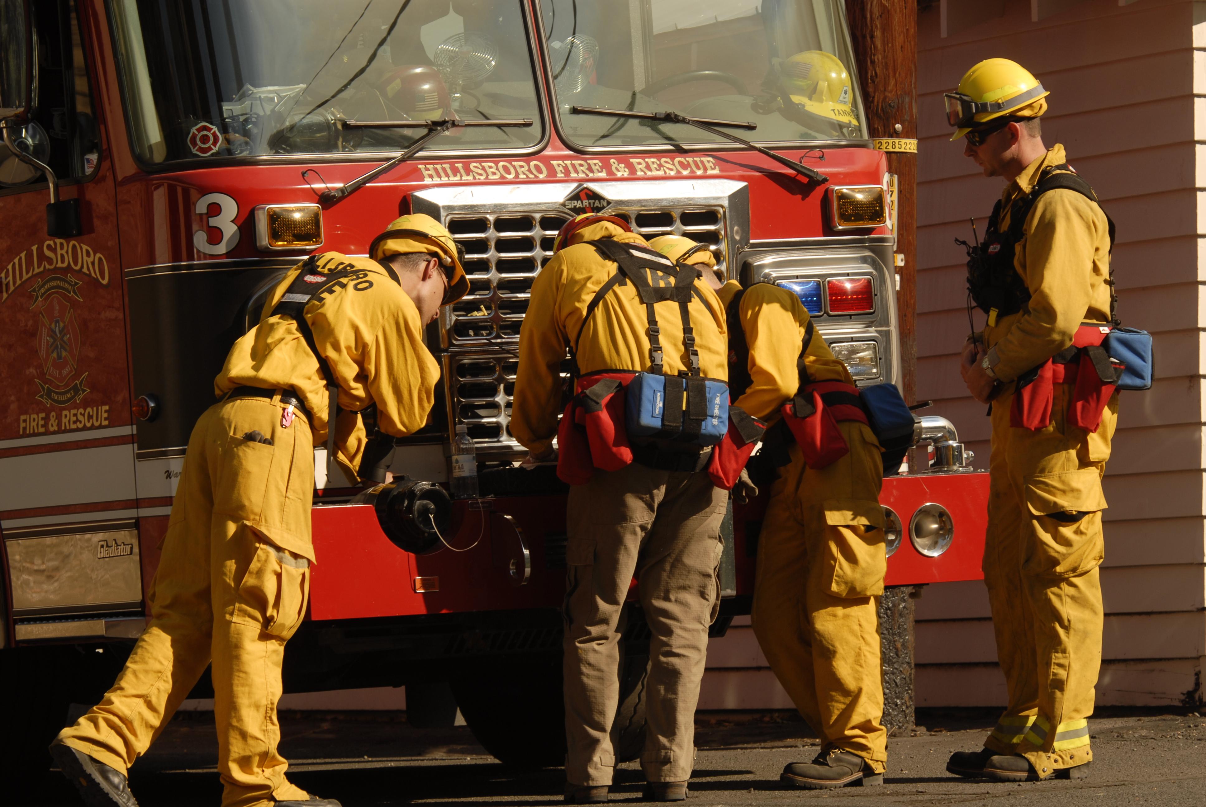 Four firefighters in yellow protective gear stand before a red Hillsboro Fire and Rescue engine.