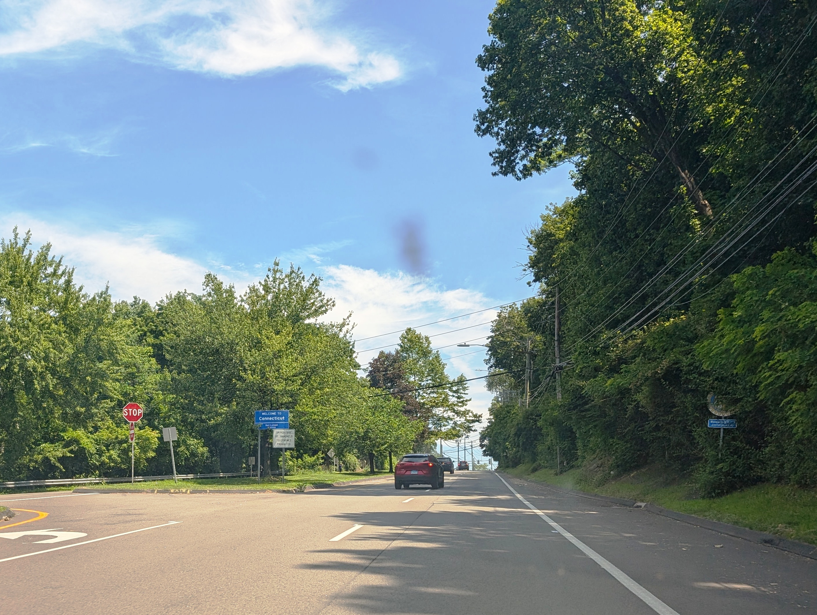 Two-lane road with double yellow center line, stop sign, and utility poles in Greenwich, Connecticut.