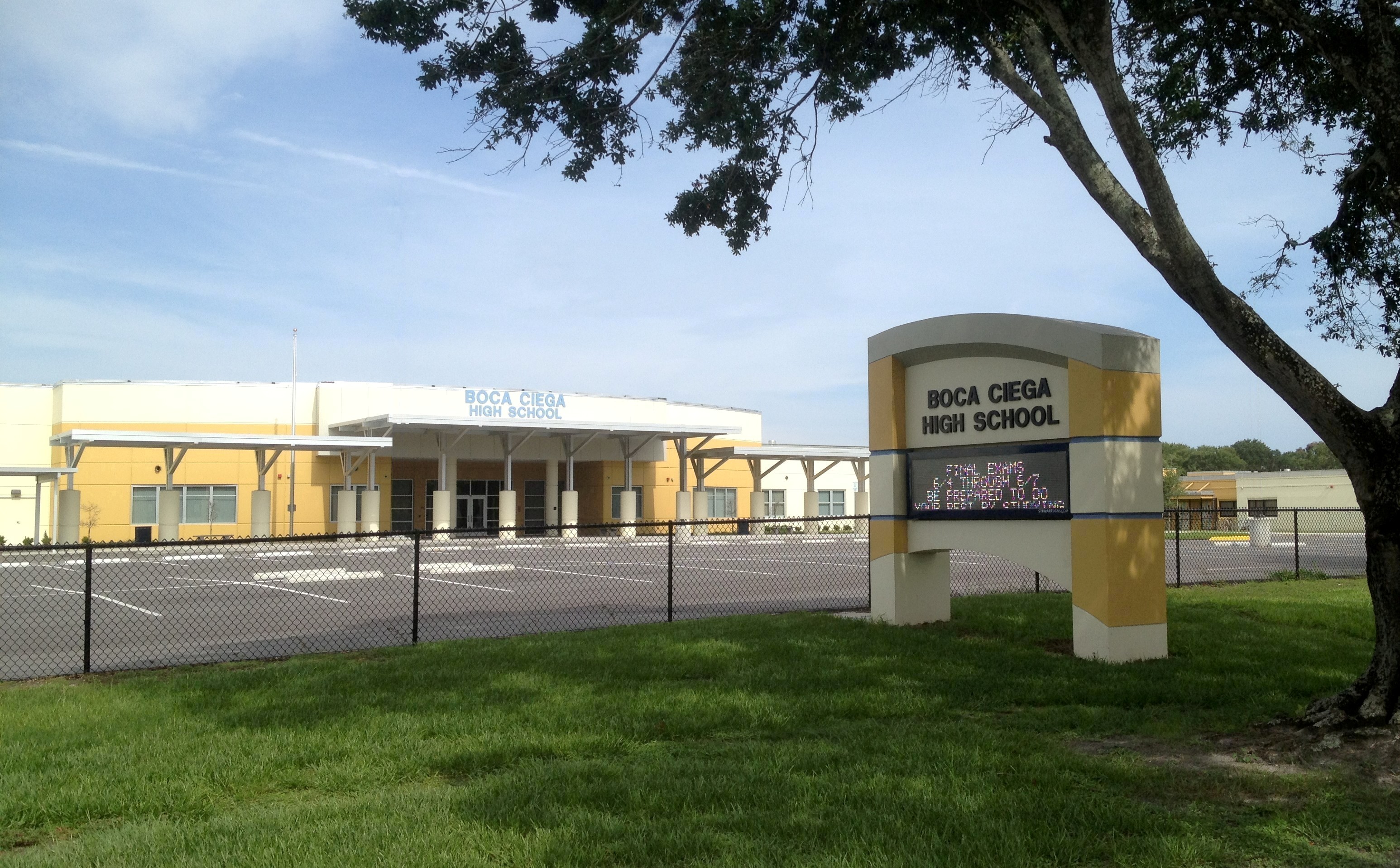 Exterior of a yellow and white school building with a monument sign reading Boca Ciega High School.