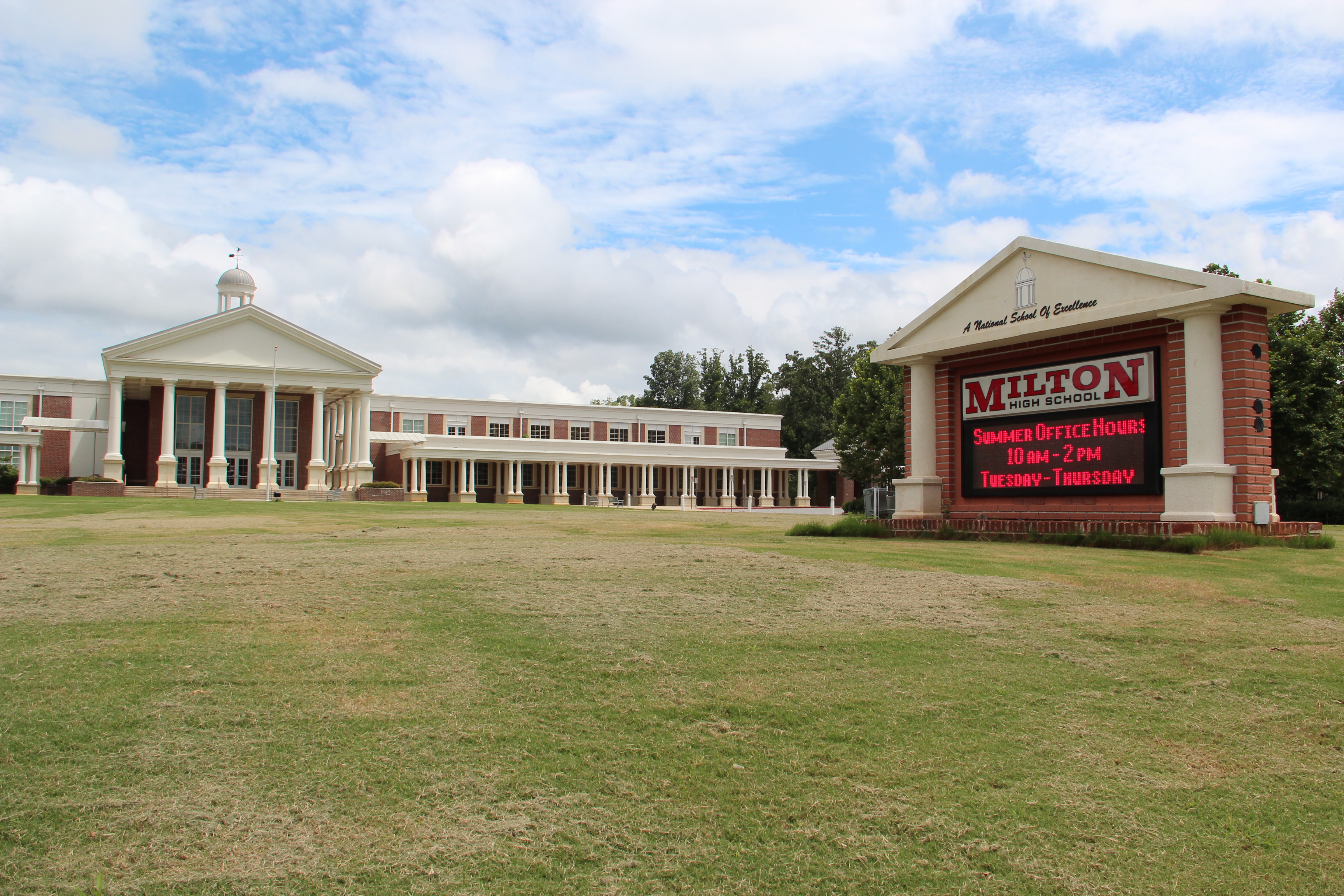 Brick school building with white columned entrance and a sign reading Milton in front.