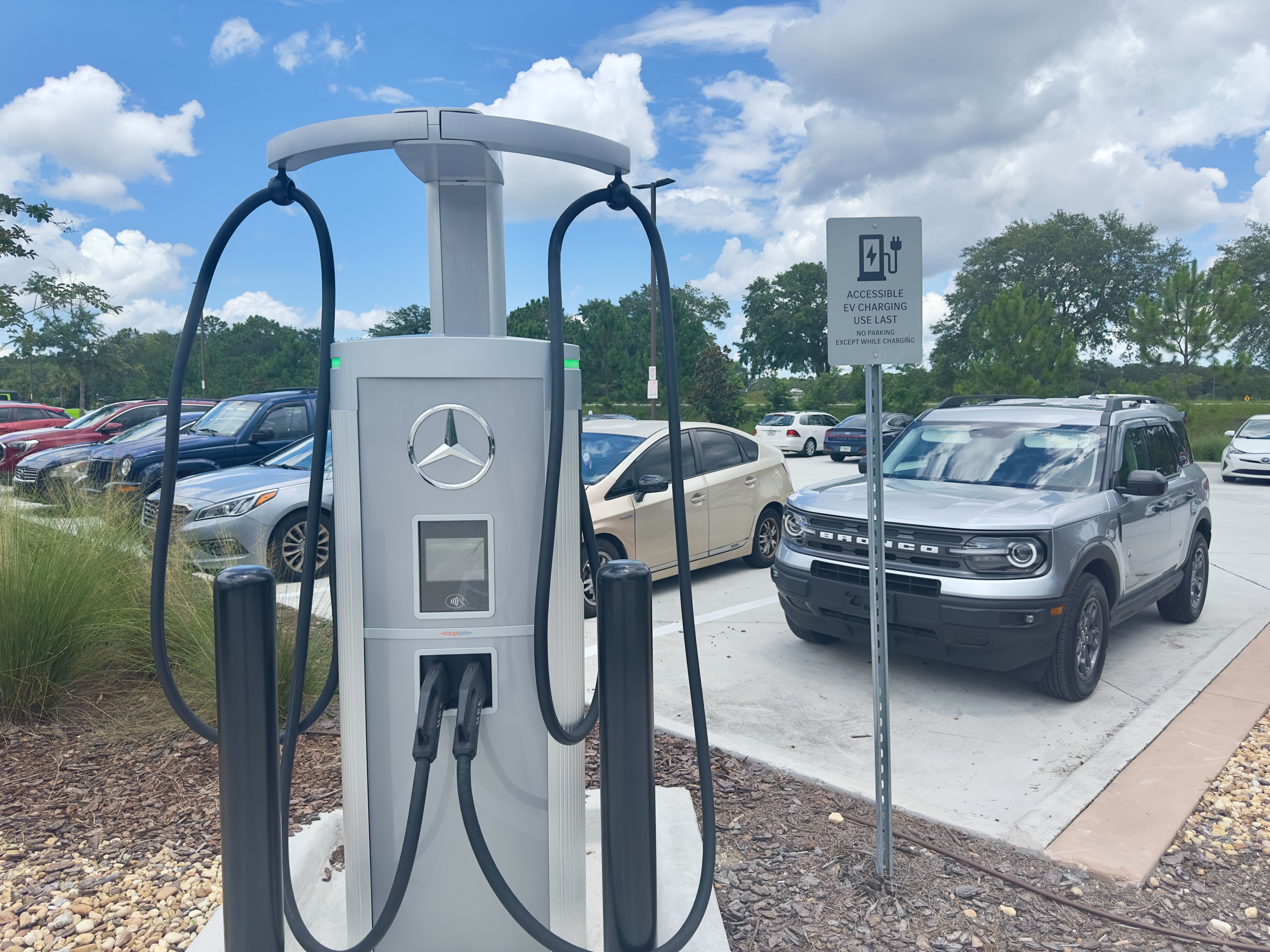 Dual-port EV charging station on a pedestal in a parking lot.