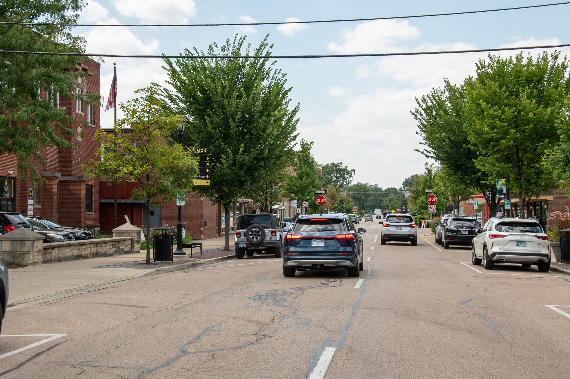 Cars travel along a tree-lined downtown street past brick commercial buildings.