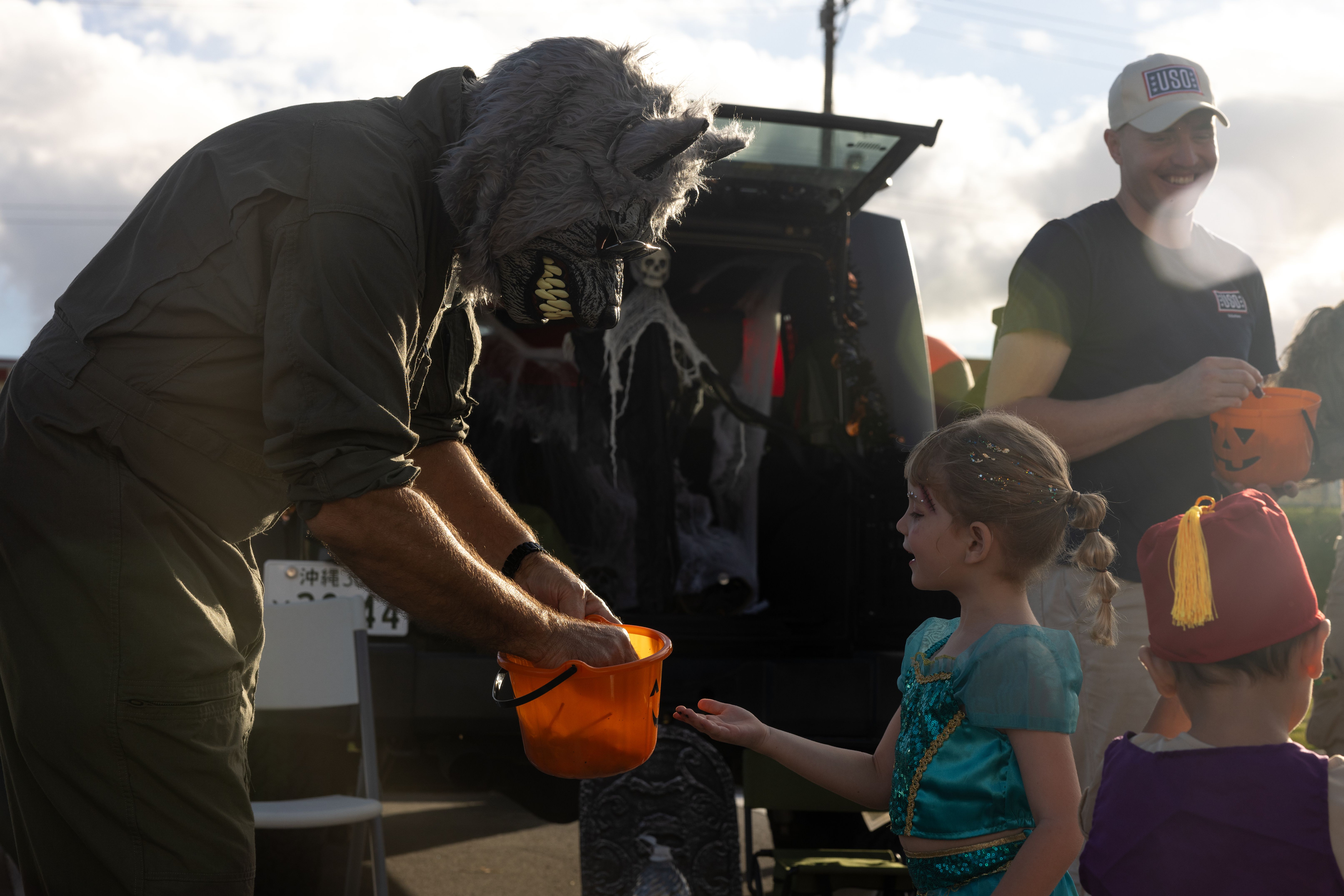 An adult in a monster costume hands candy to a costumed child outdoors.