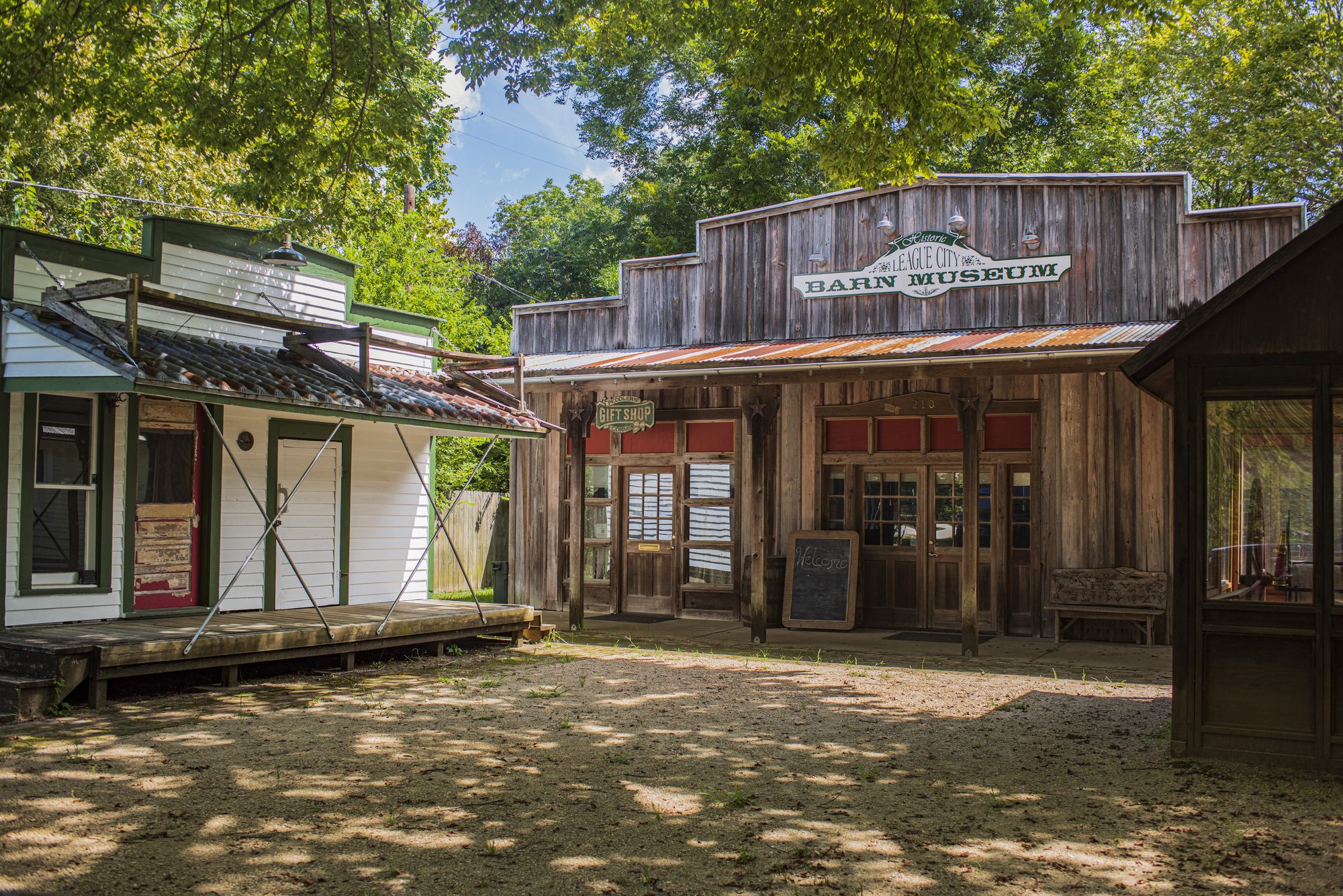 Weathered wooden storefronts with corrugated metal roofs around a shaded dirt courtyard.