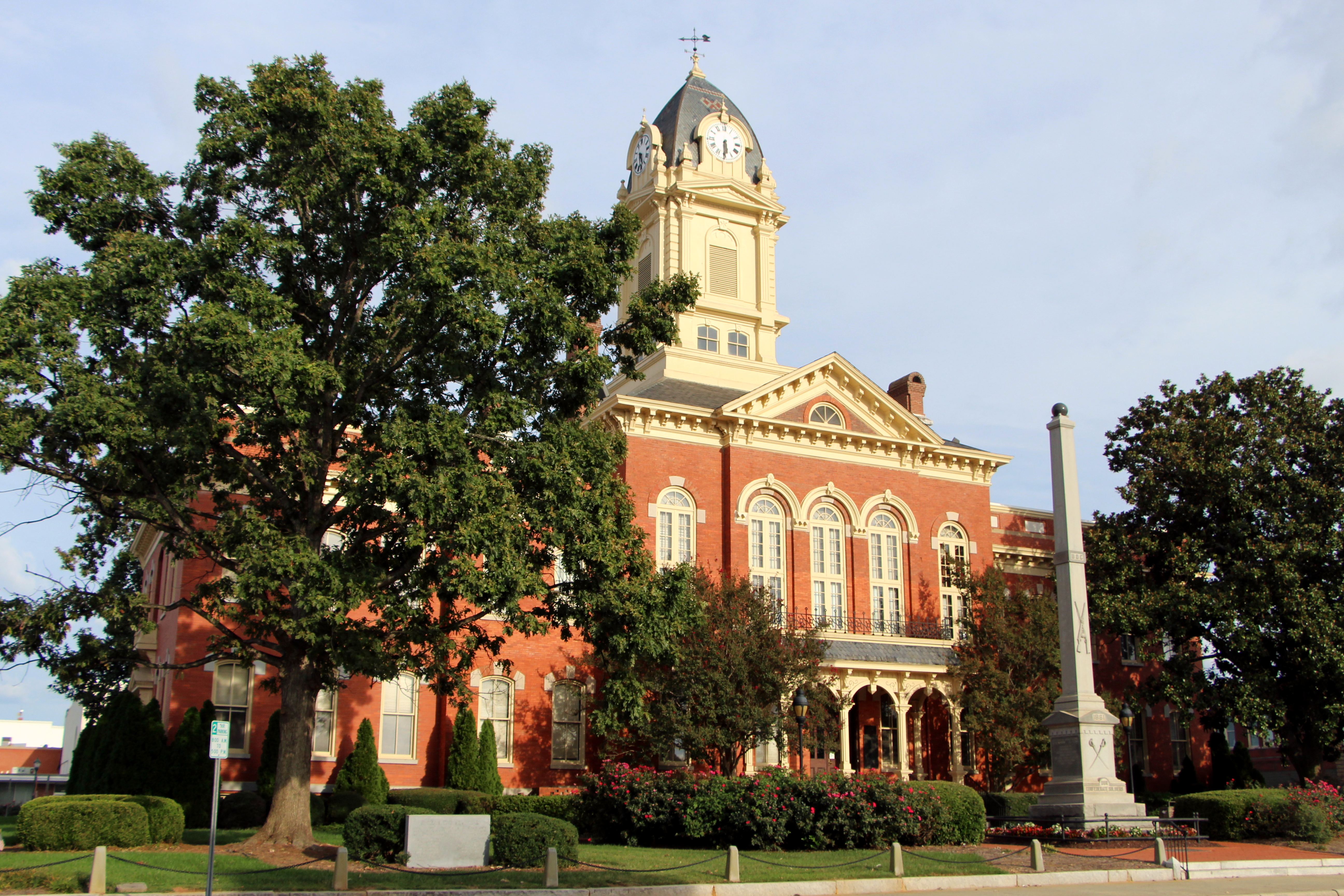 Historic red-brick courthouse with a clock tower and obelisk monument out front.