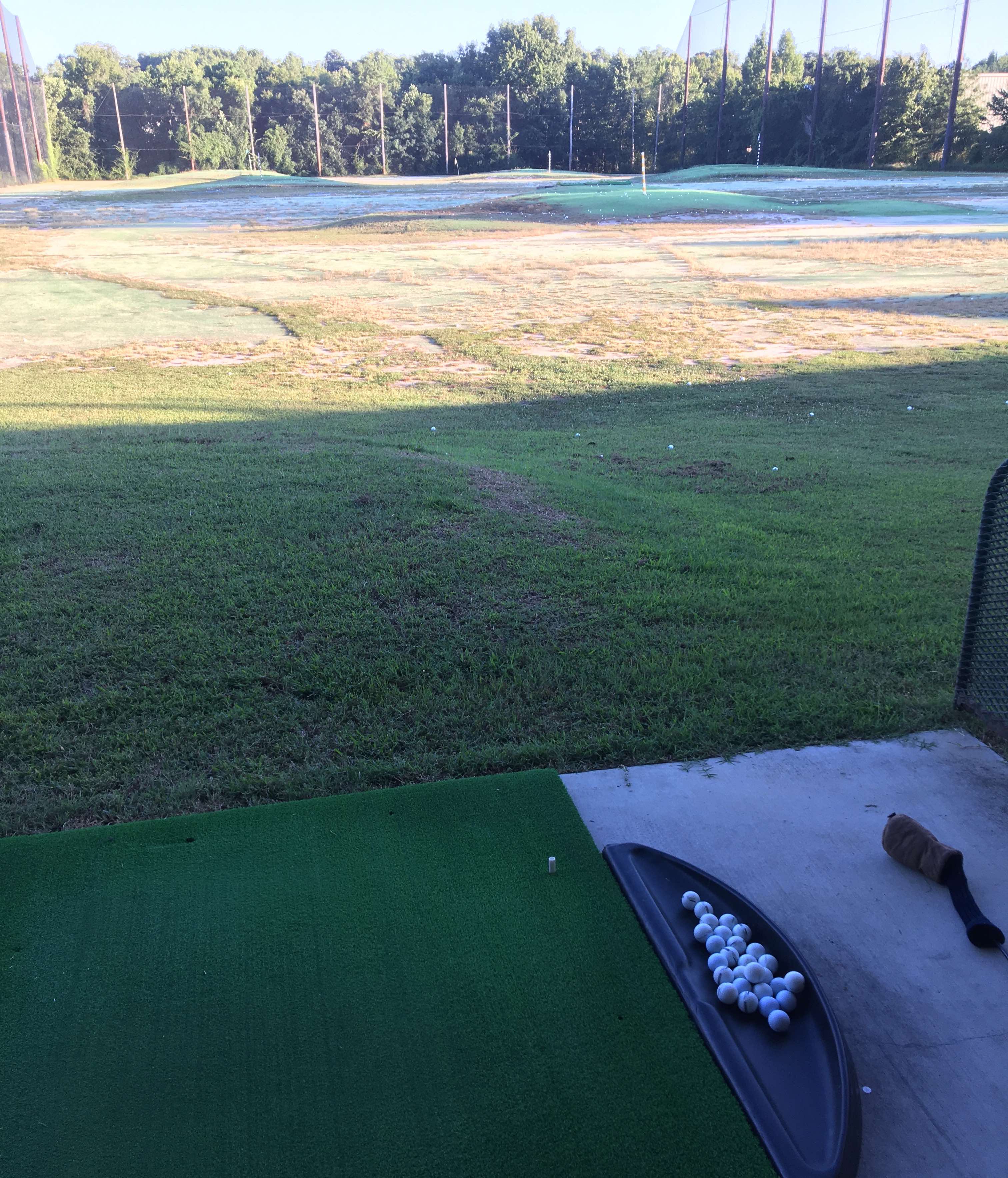 A golf tee mat with a tray of white golf balls and a club at a driving range.