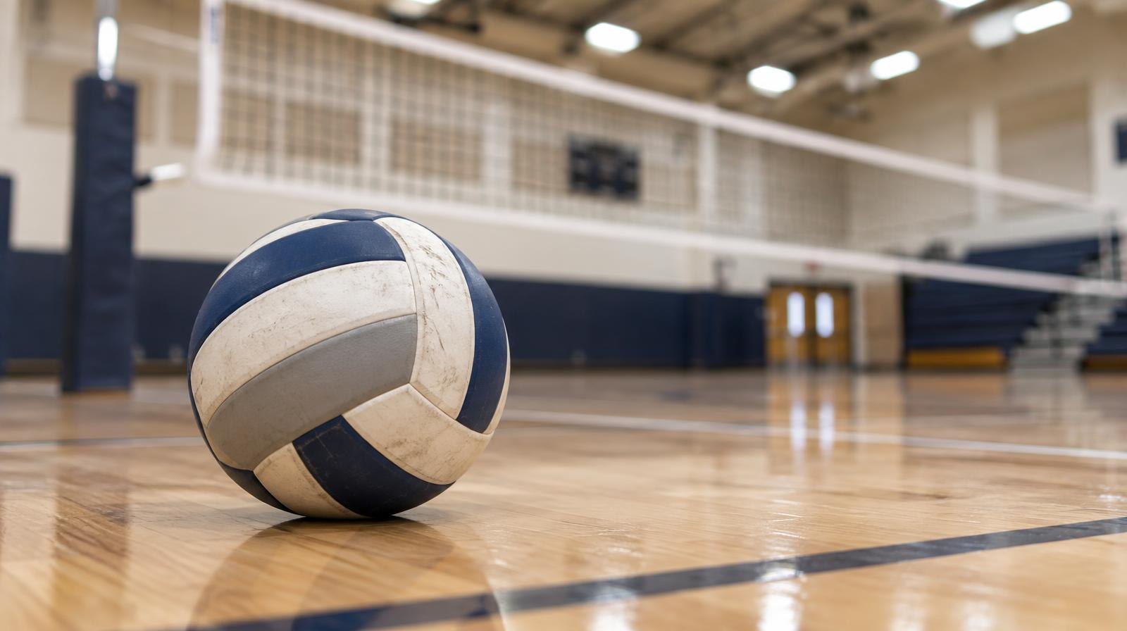 A volleyball resting on a hardwood gymnasium floor near the net.