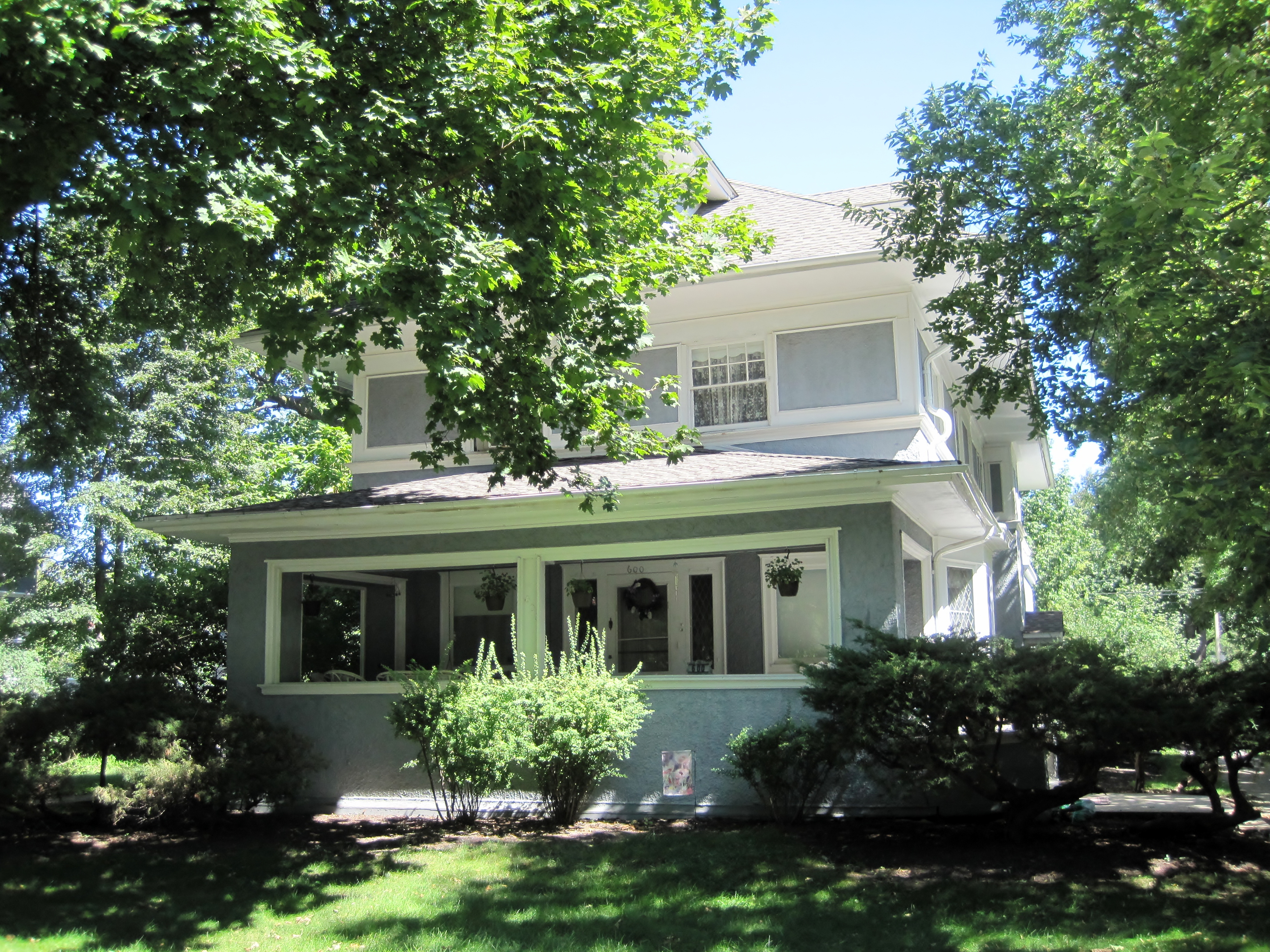 Two-story white craftsman house with a covered front porch and large trees.