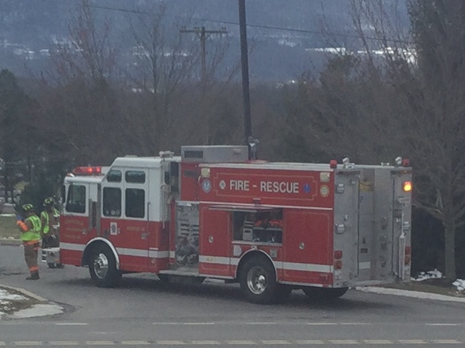 Red fire-rescue engine parked on a road with a firefighter in high-visibility jacket nearby.