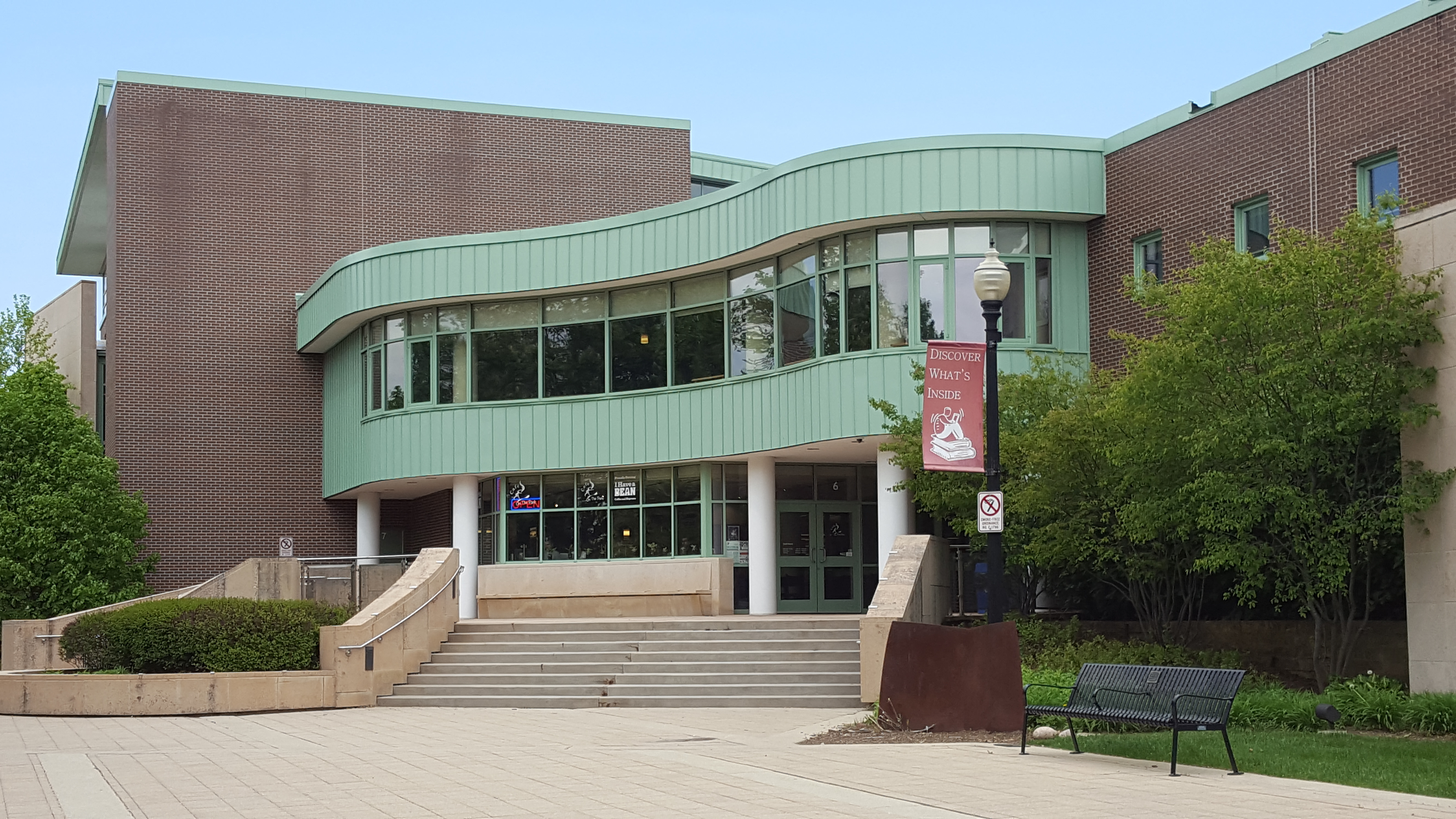 Exterior view of the Wheaton Public Library building showing a curved glass entrance and brick facade.