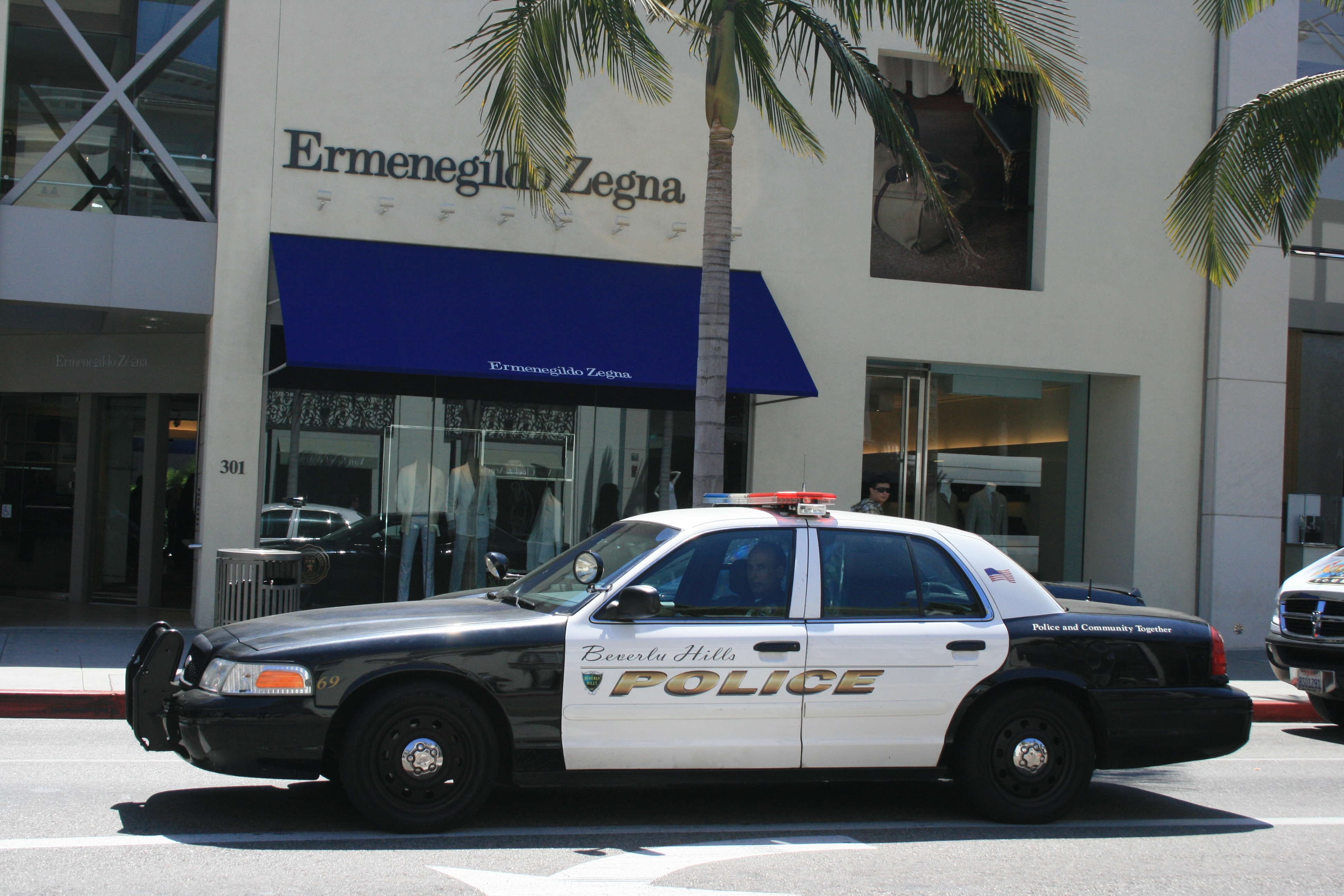 Beverly Hills Police Department patrol car parked on a street with palm trees nearby.