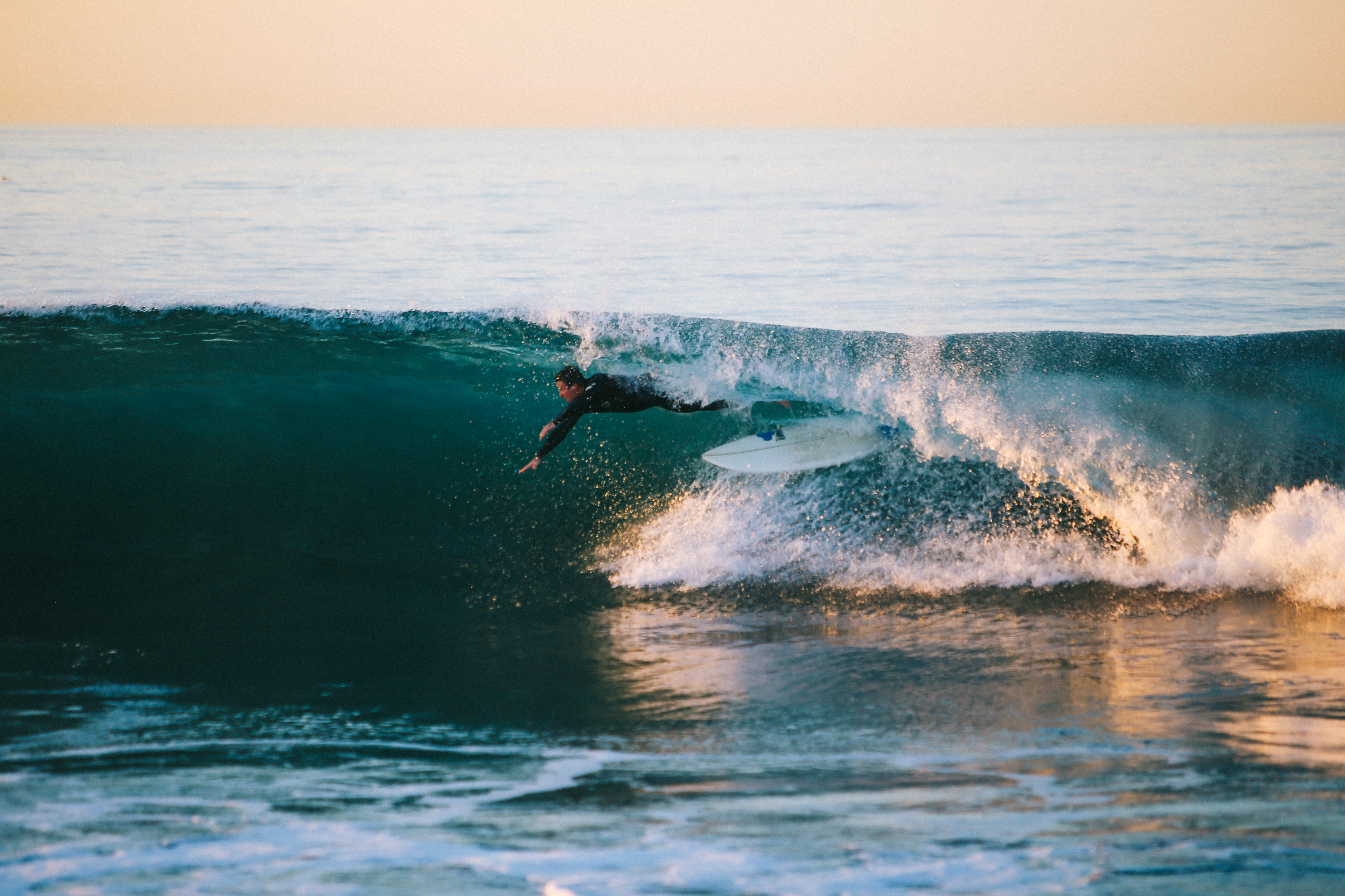 A surfer in a wetsuit rides inside a large barreling ocean wave.