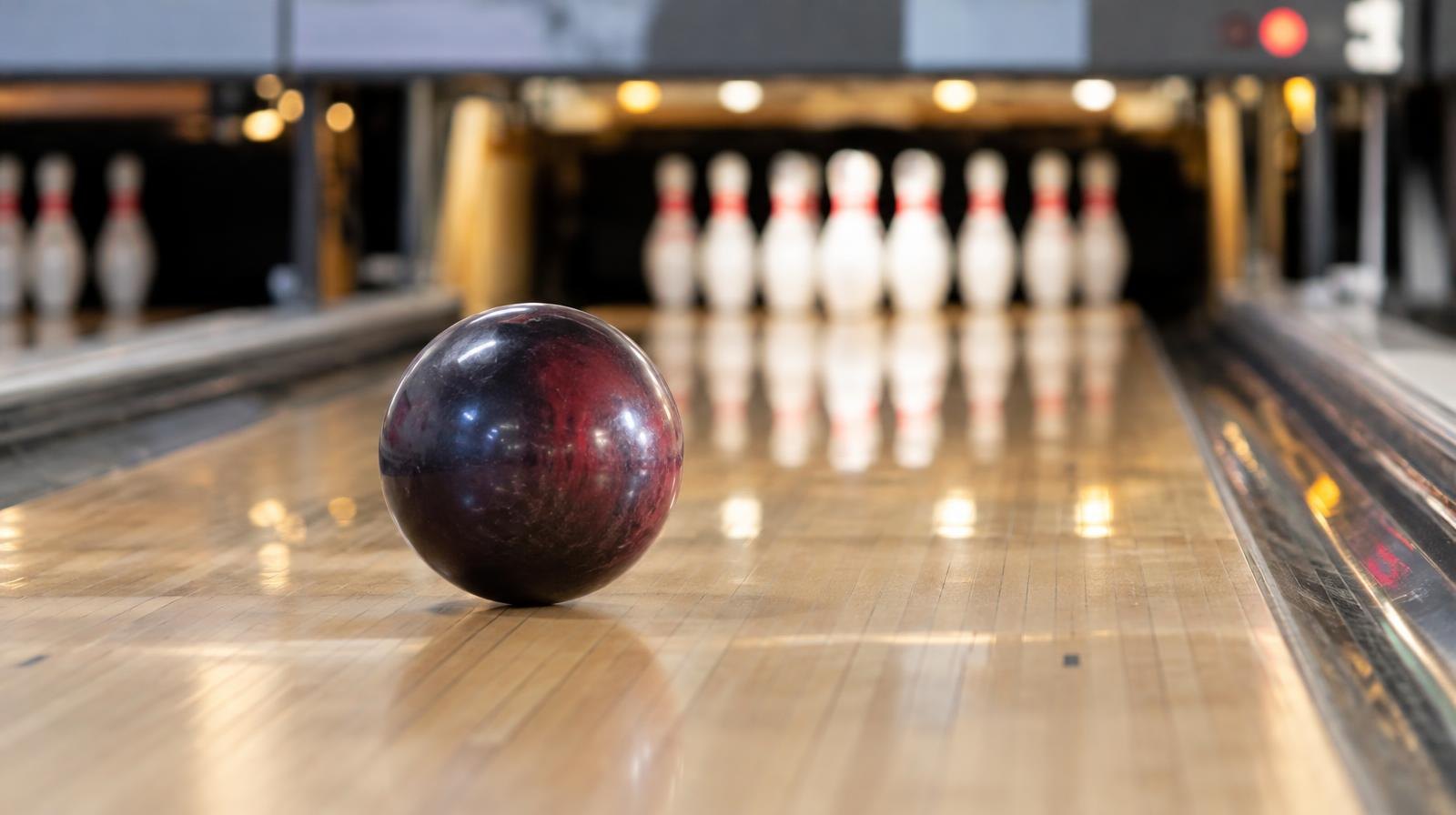 A shiny bowling ball rolling down a hardwood lane toward white pins at the far end.